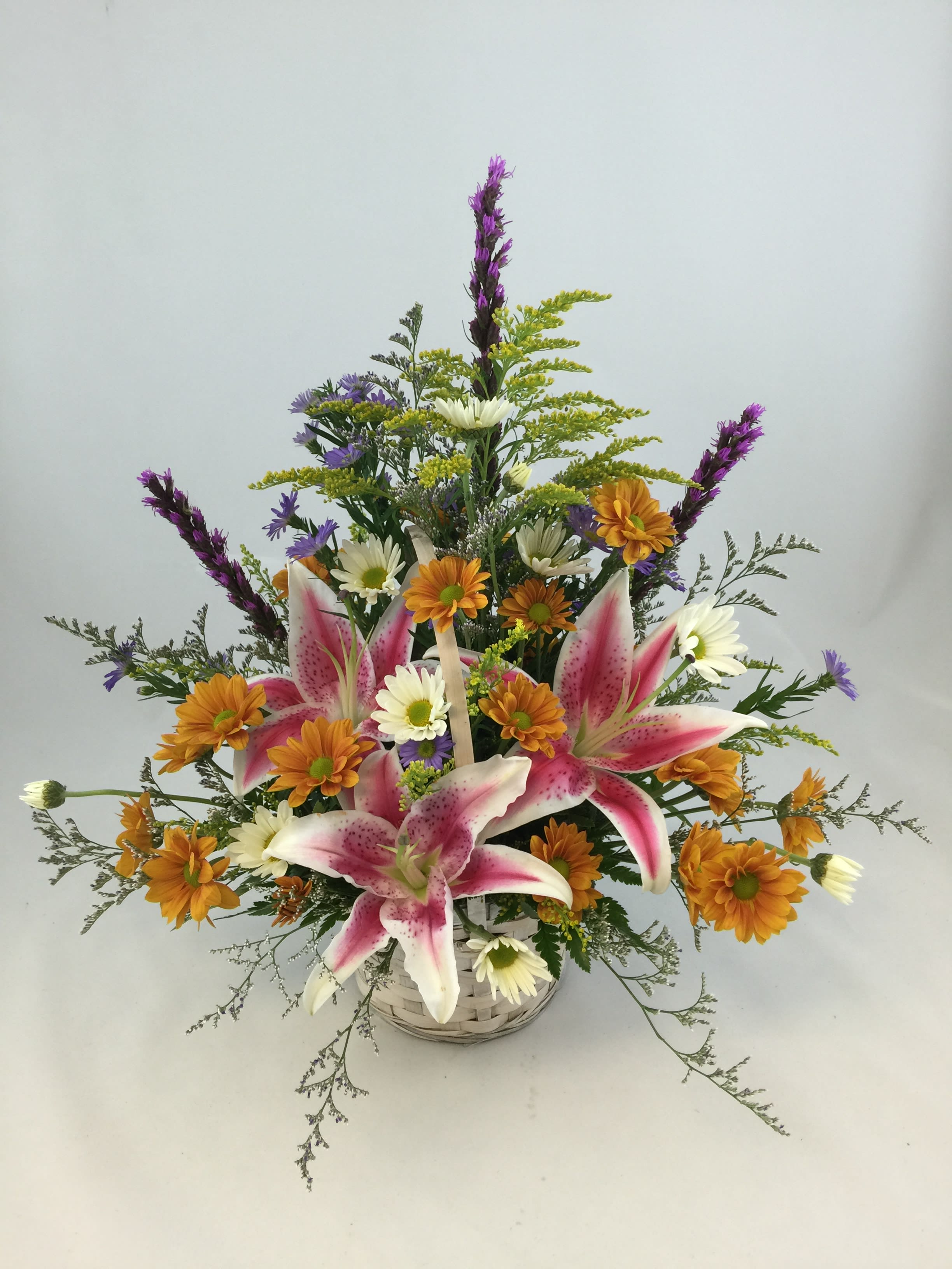 Basket arrangement with pink lilies, orange daisies, and purple accents