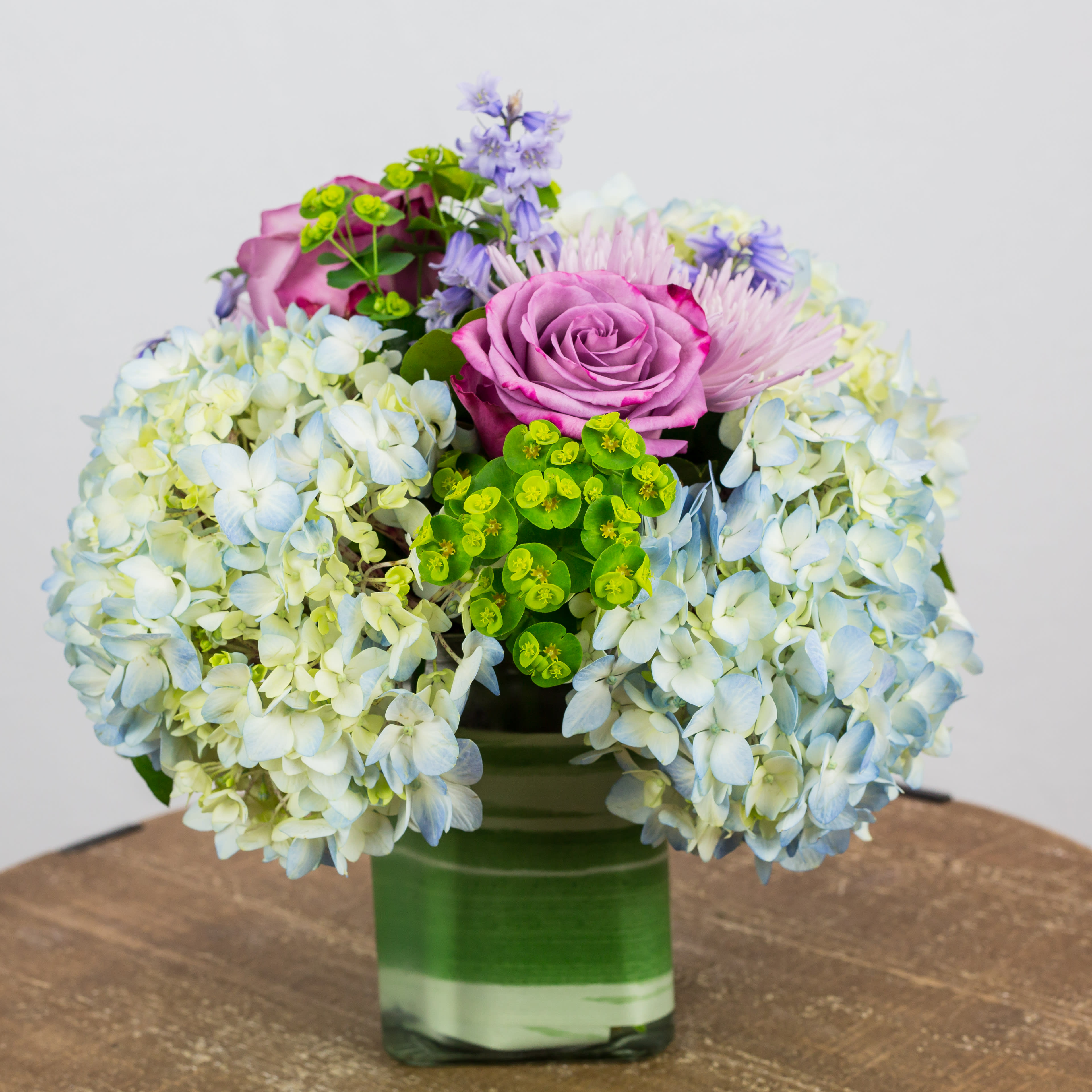 Pink roses and blue hydrangeas in a green glass vase