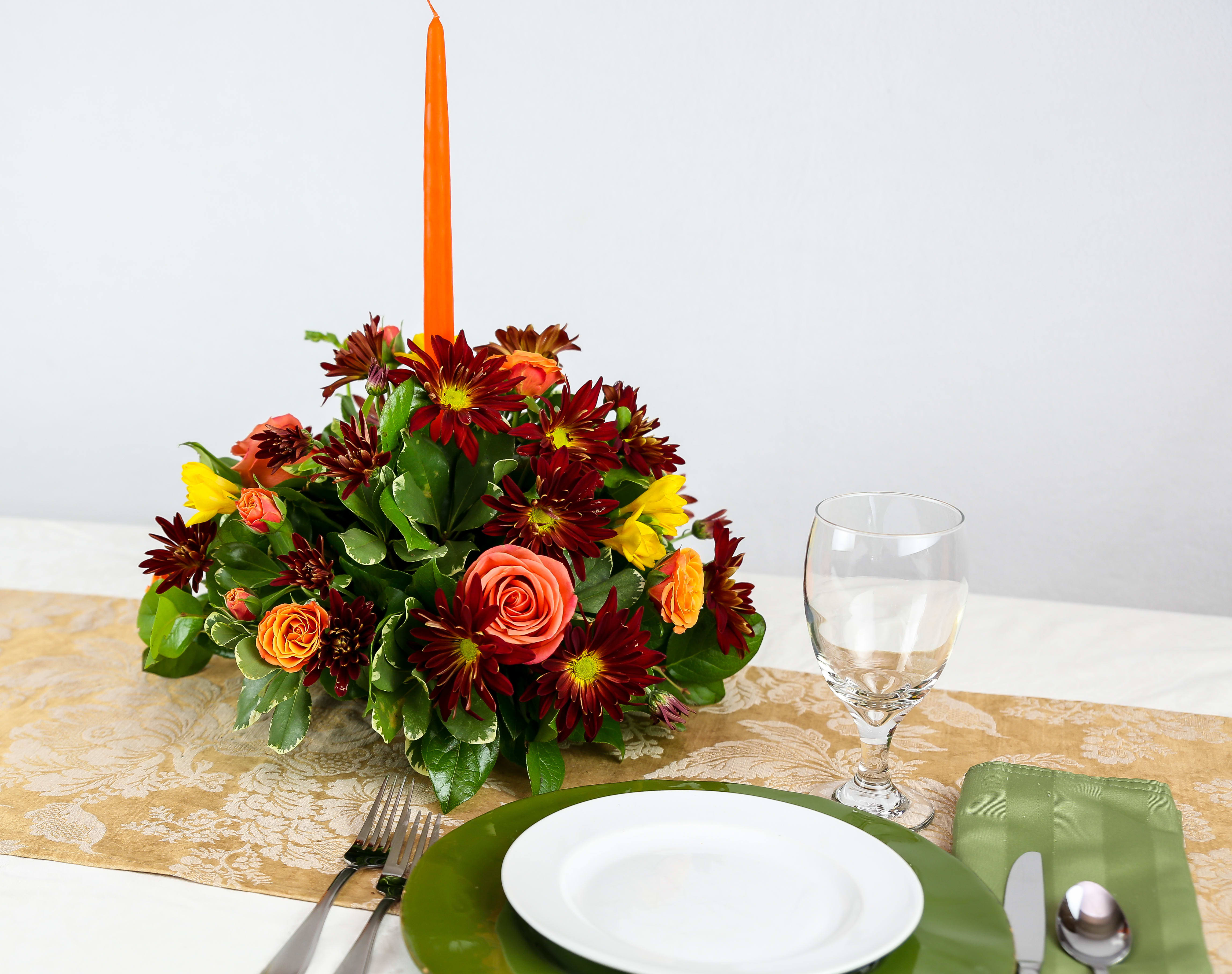 Autumn floral centerpiece with a tall orange candle on a table setting
