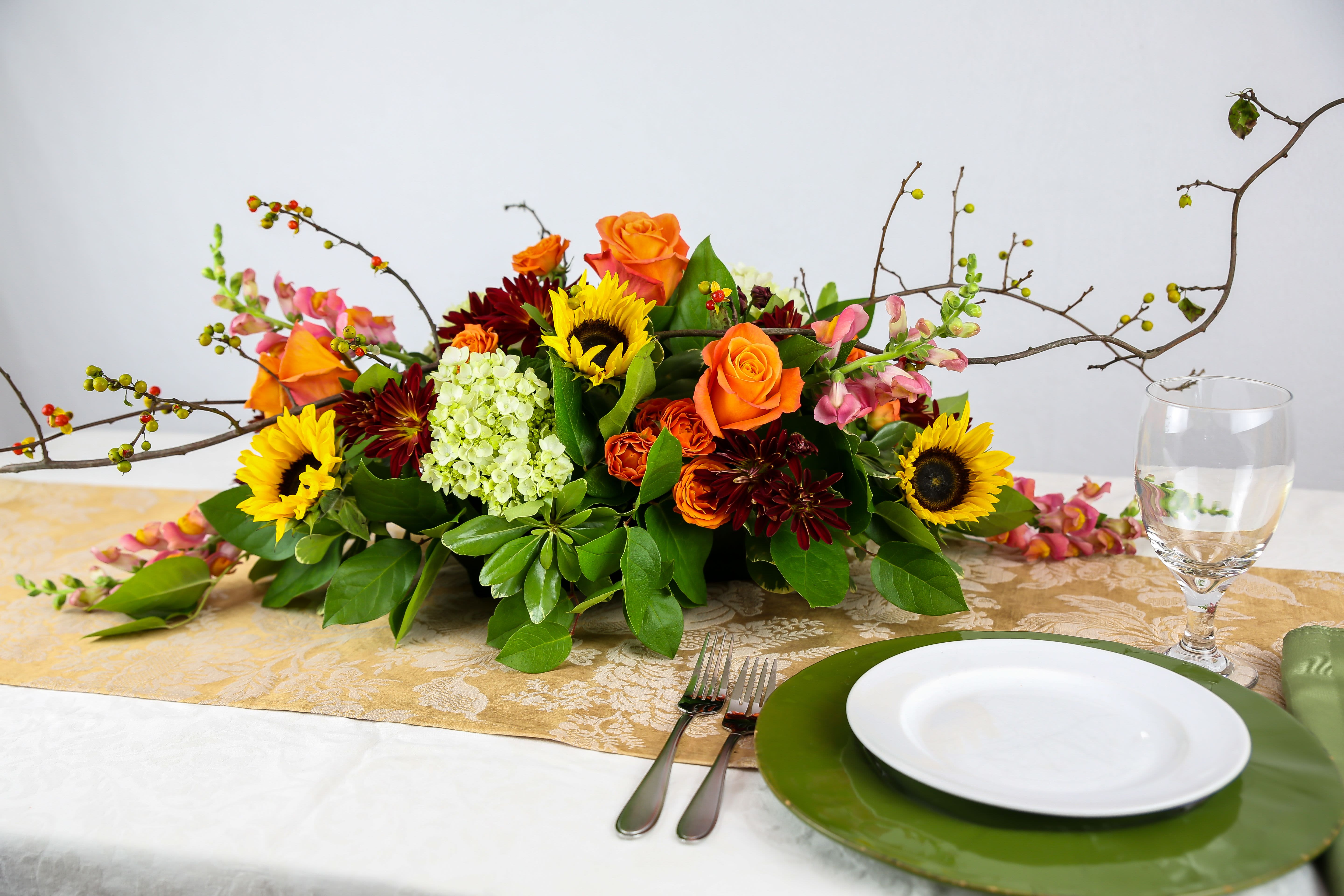 Low floral centerpiece with sunflowers, orange roses, and burgundy blooms on a table