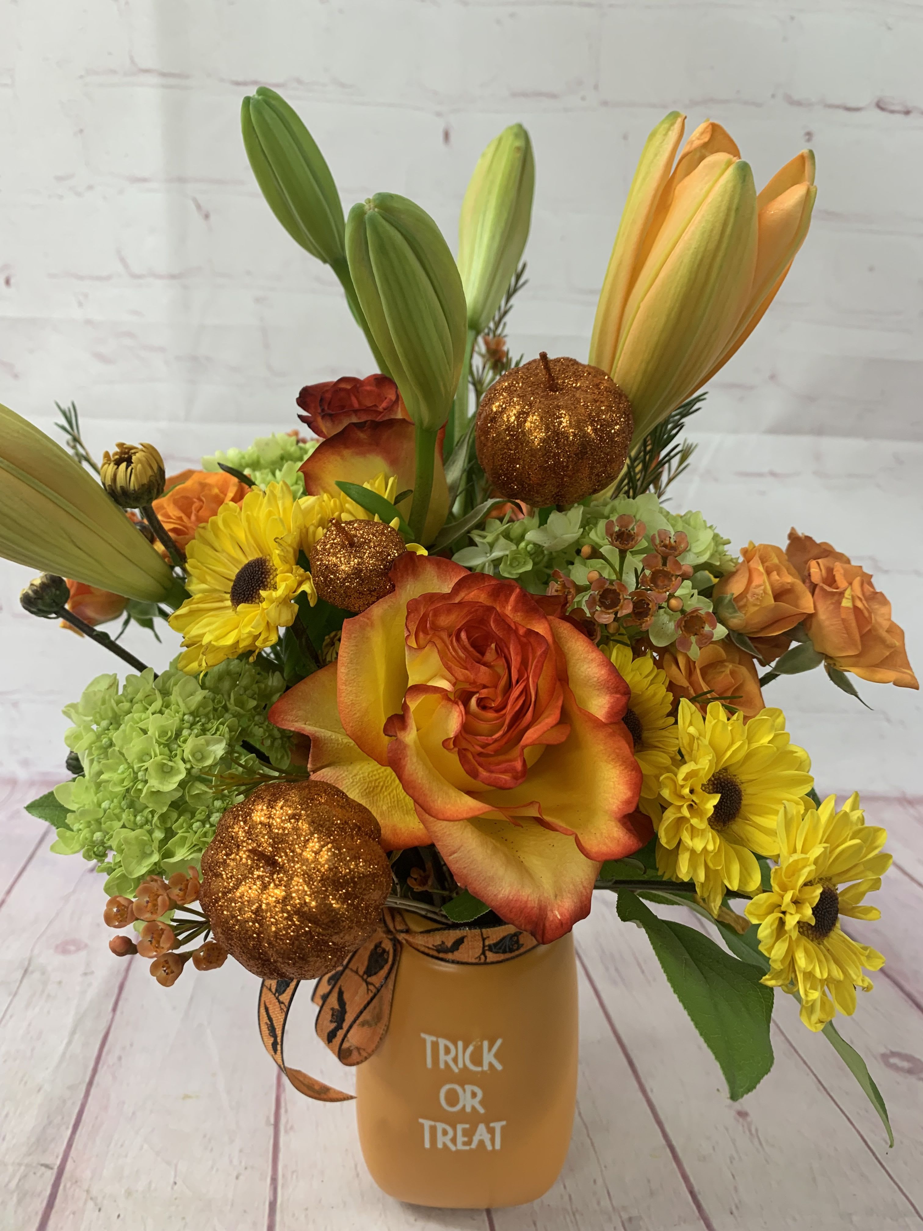 Halloween bouquet with orange roses, yellow daisies, lilies, and glitter pumpkins in a Trick or Treat vase
