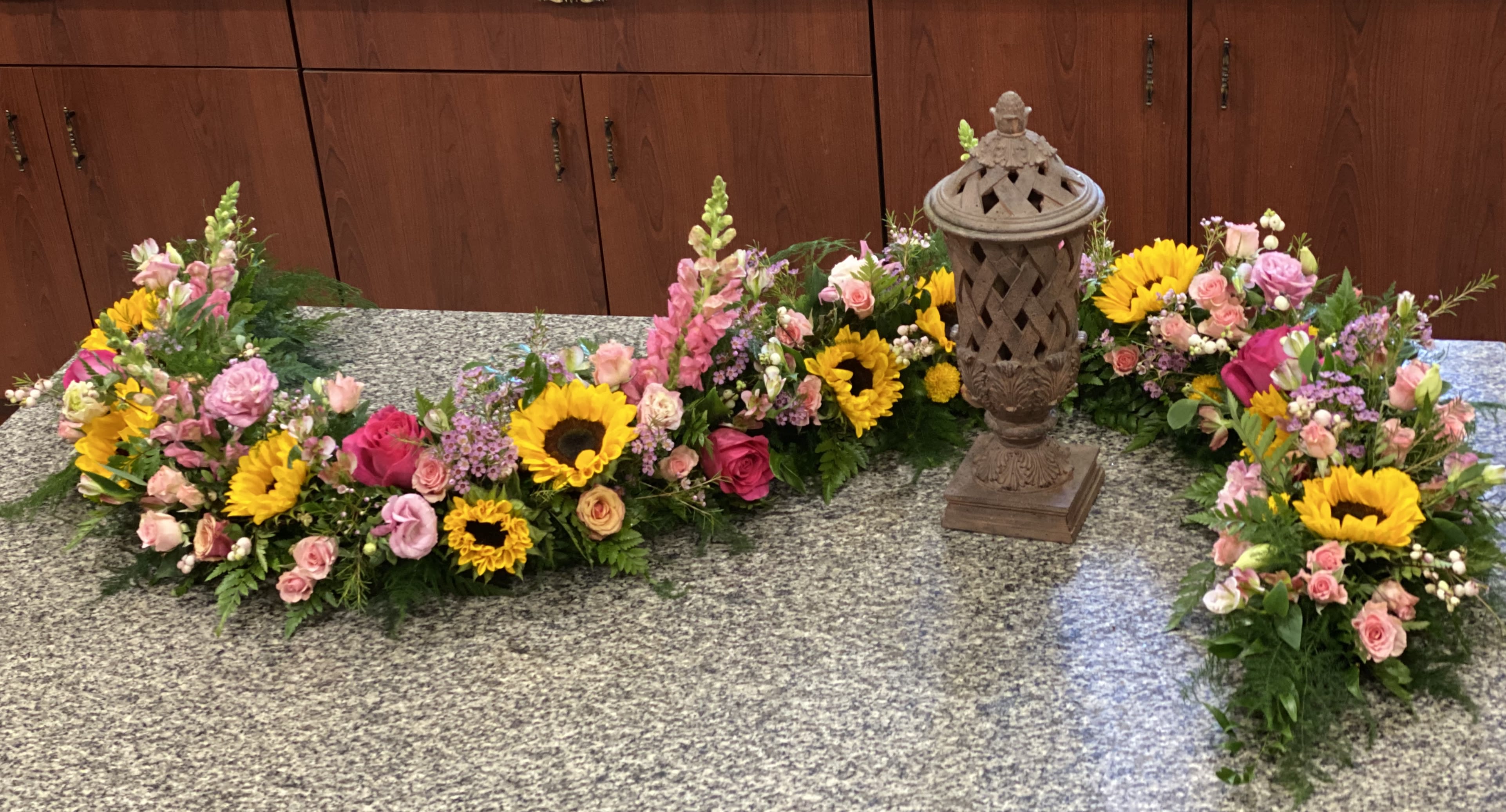 Floral funeral arrangement with sunflowers, pink roses, and snapdragons around a lantern