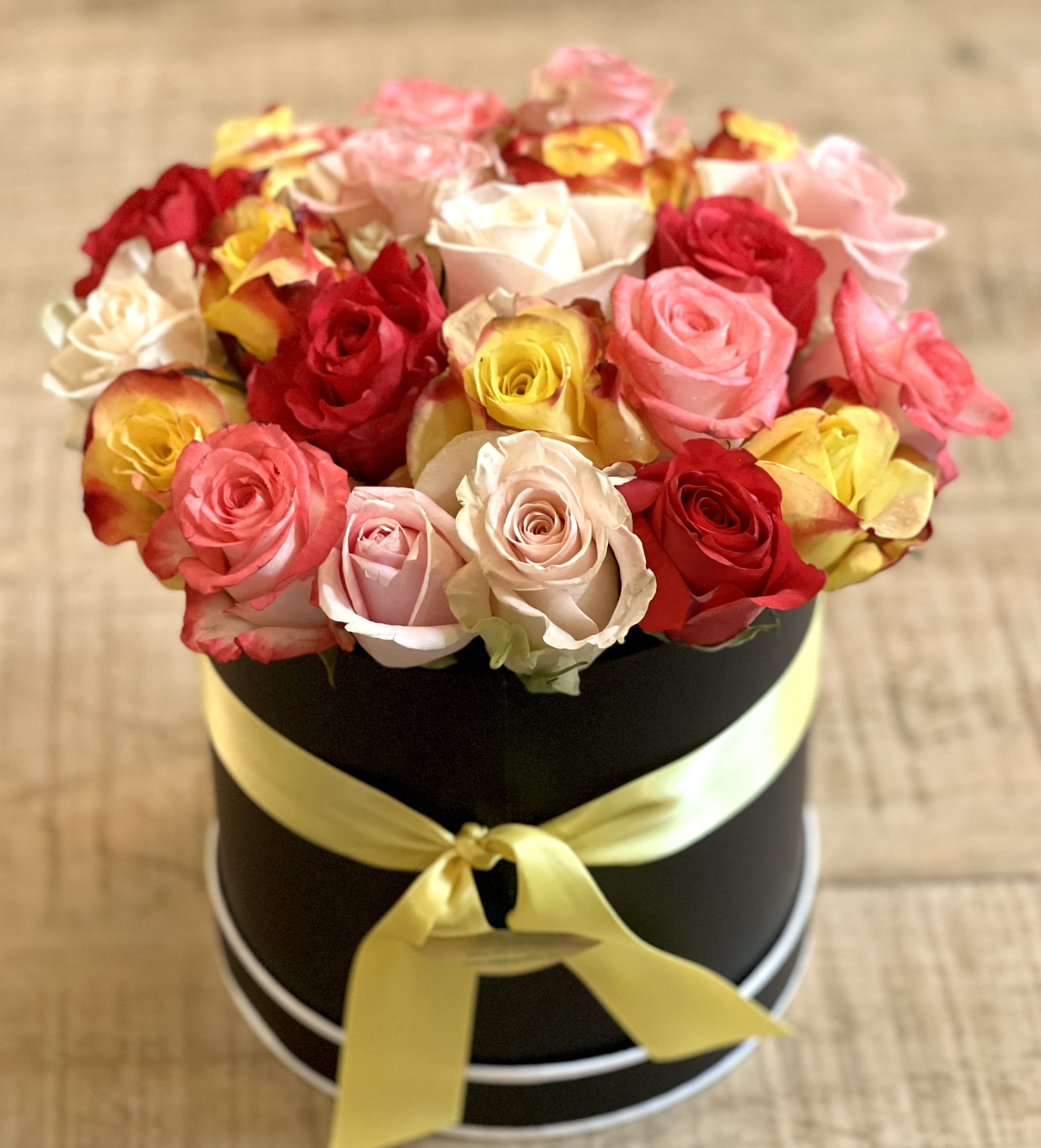 Round box of multicolored roses tied with a yellow ribbon
