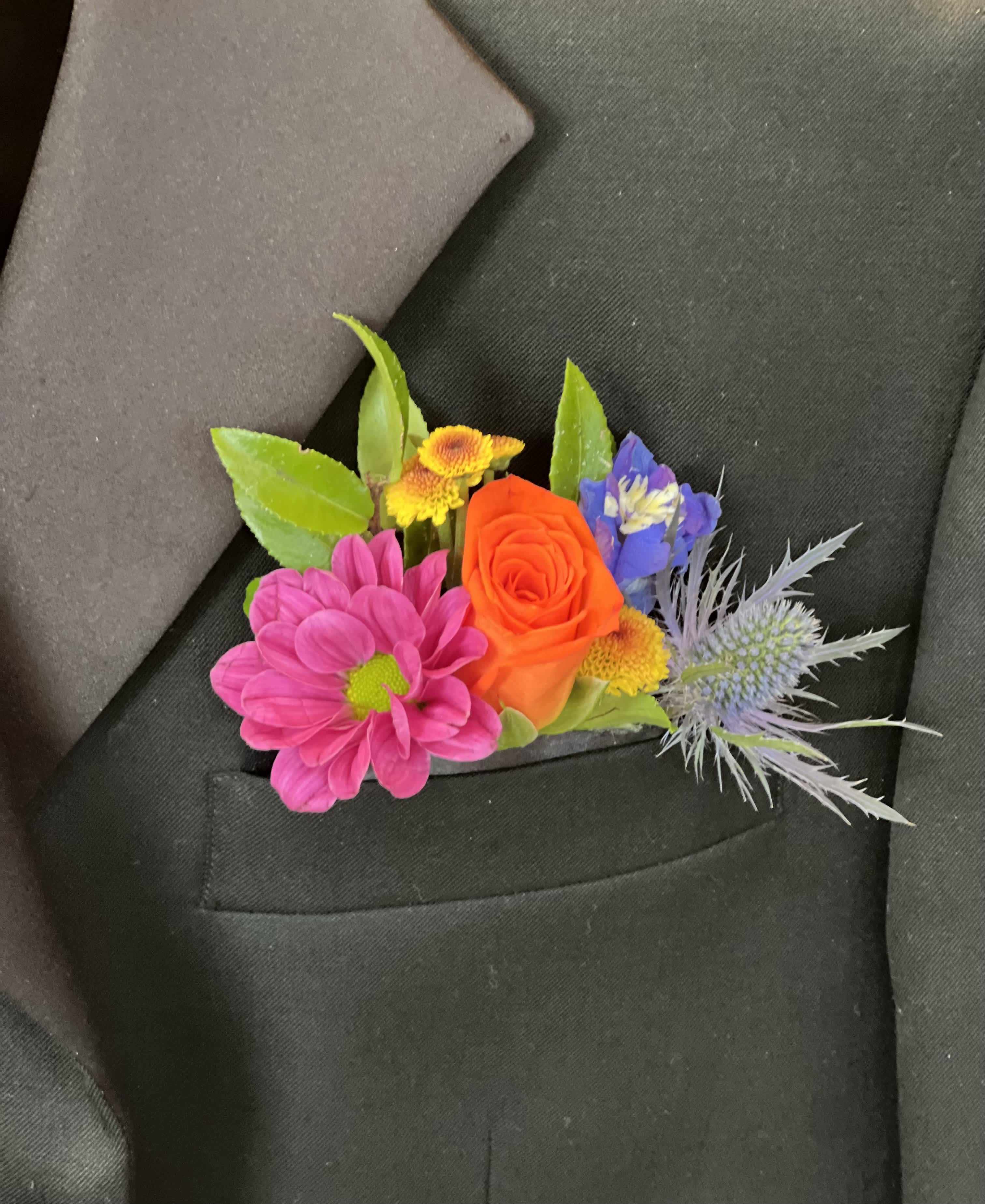 Colorful boutonniere with pink daisy, orange rose and mixed blooms in a black suit pocket