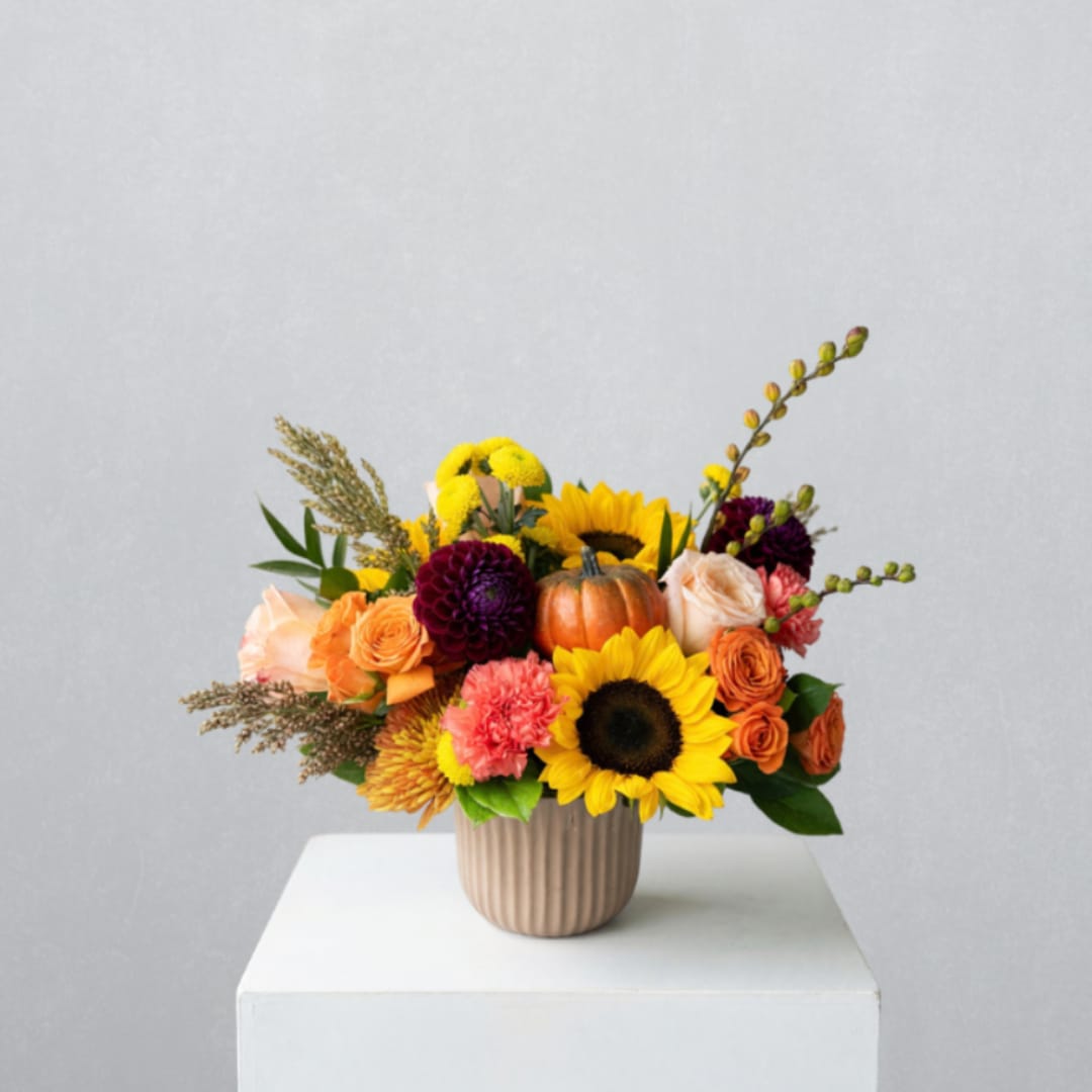 Mixed bouquet with sunflowers, roses, and a small pumpkin in a ribbed vase