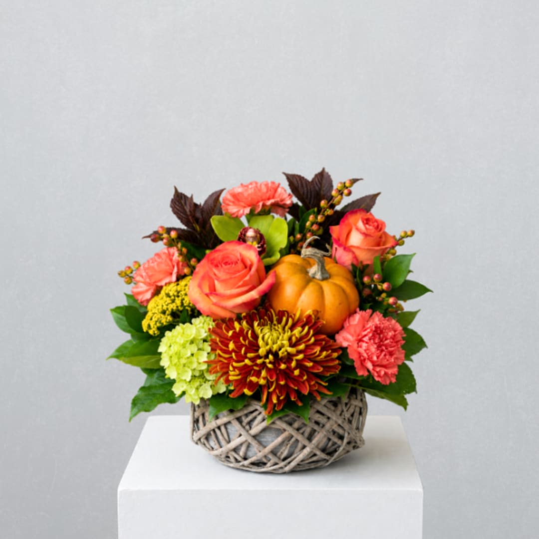 Autumn floral arrangement in a woven basket with a small pumpkin