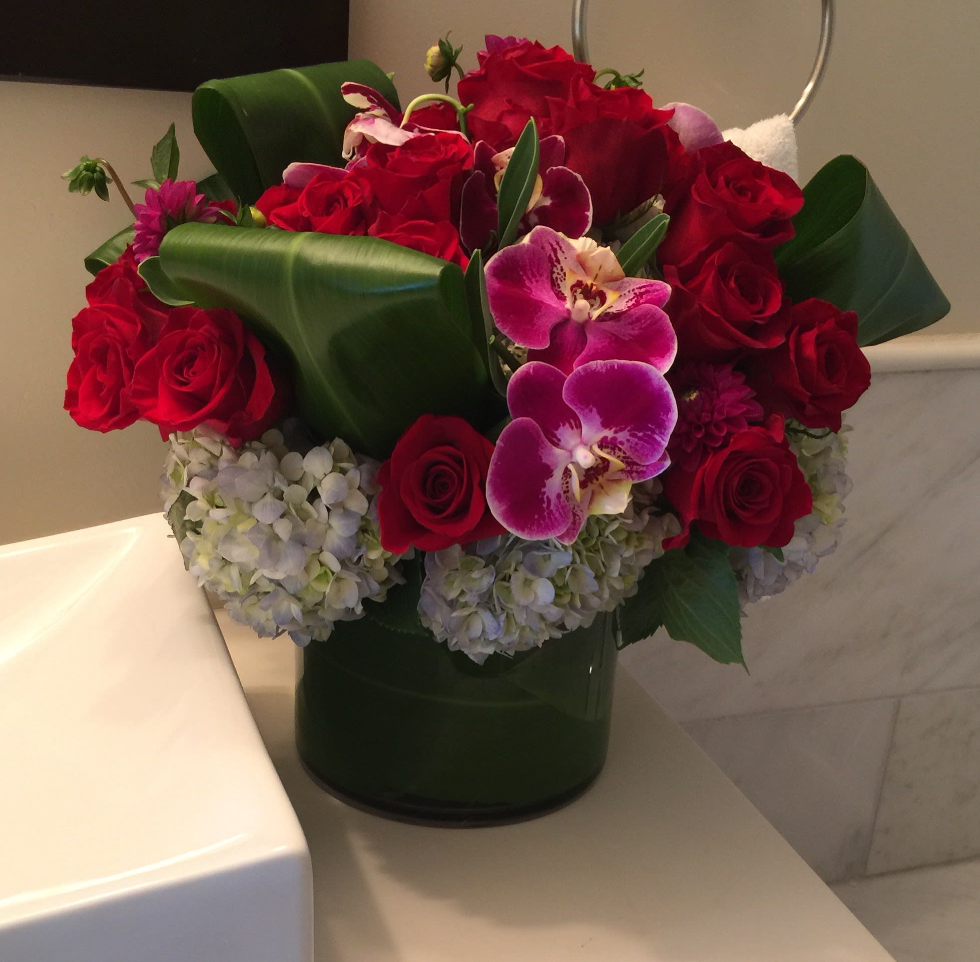Bouquet of red roses, purple orchids, and pale hydrangeas in a green vase