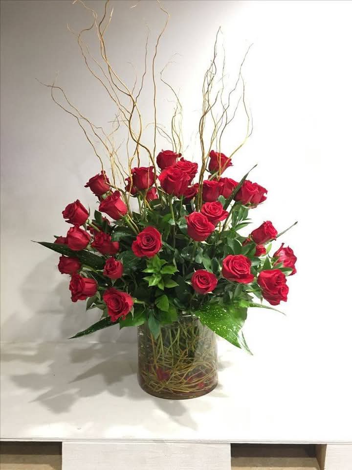 Red roses arranged in a clear glass vase with tall curly branches