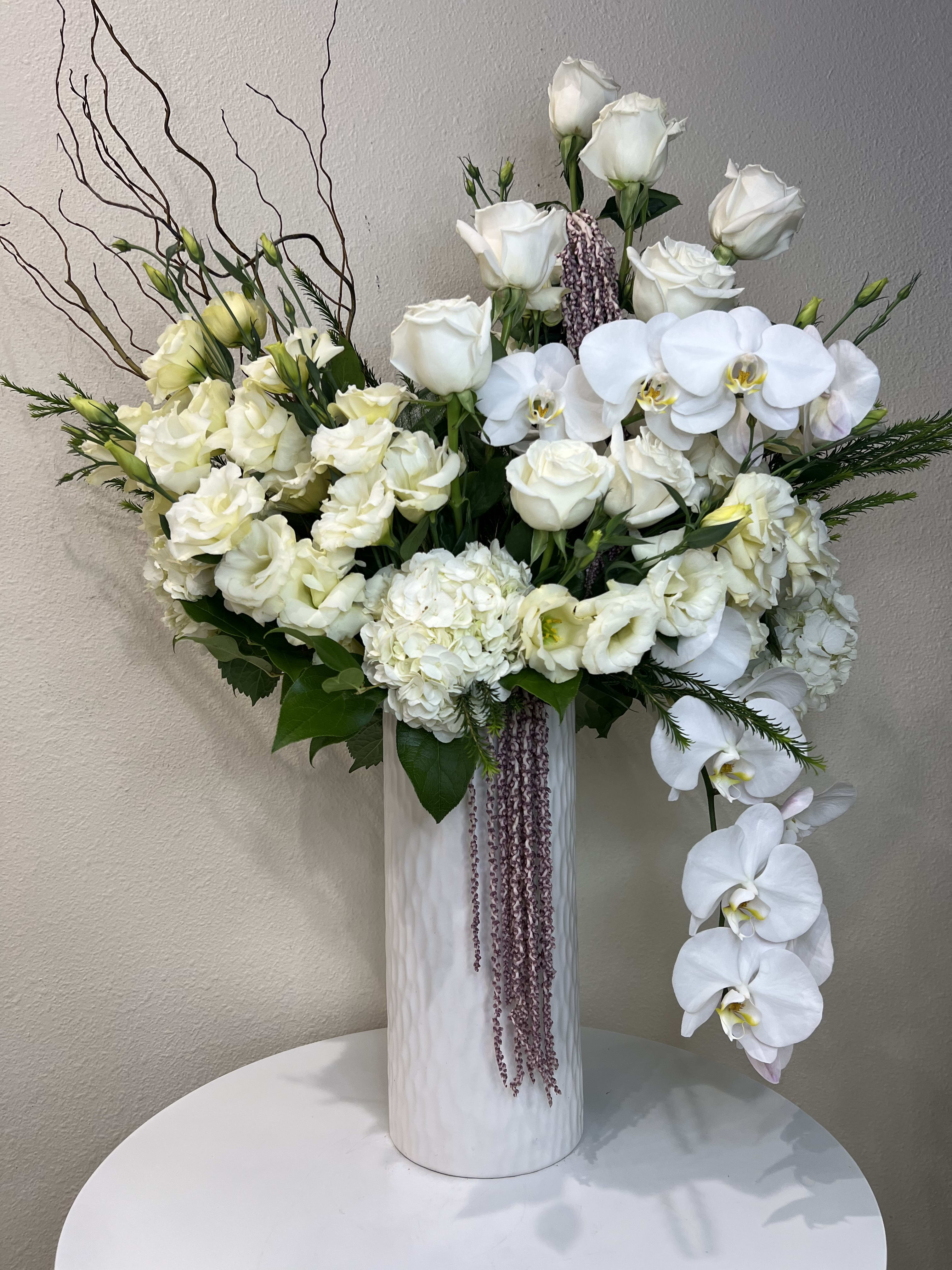 White roses and orchids arranged in a tall white vase