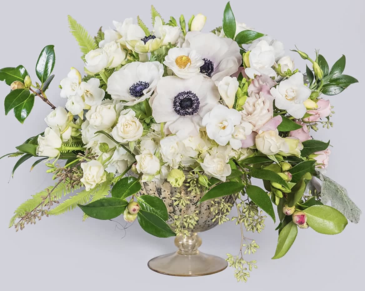 White floral arrangement in a glass compote vase with pink accents