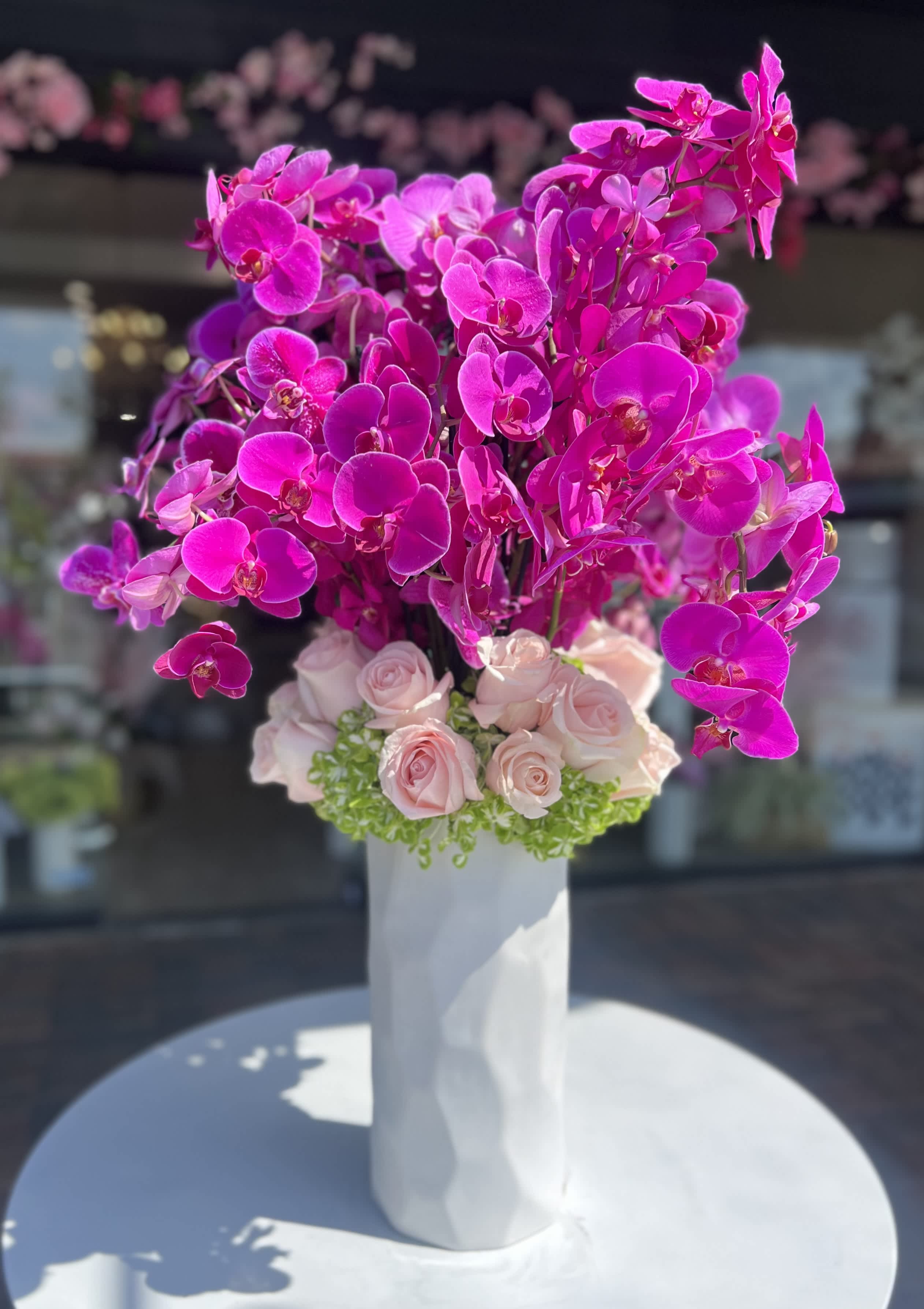 Pink orchid and pale roses arranged in a tall white vase
