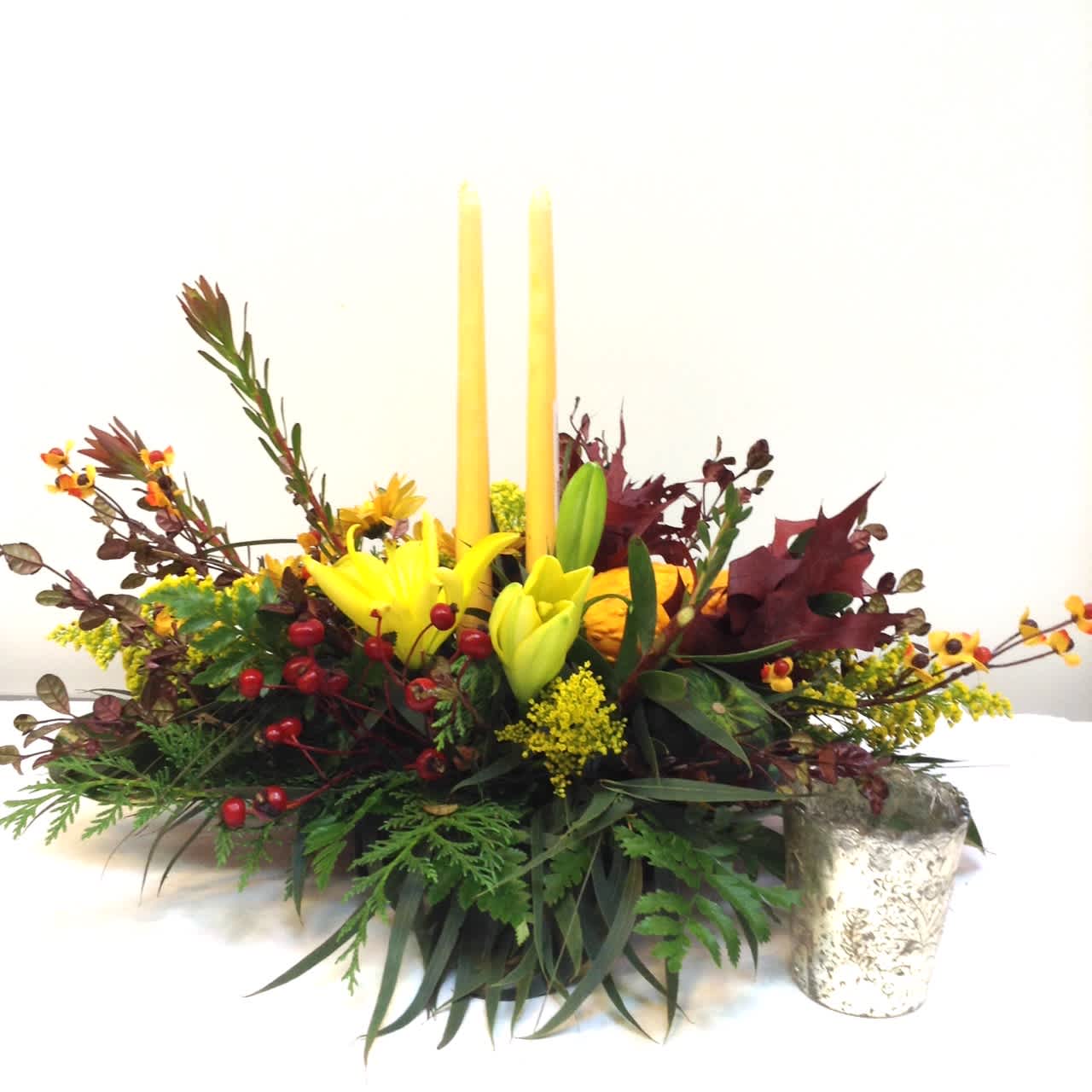 Yellow lilies in a low floral centerpiece with two tall candles