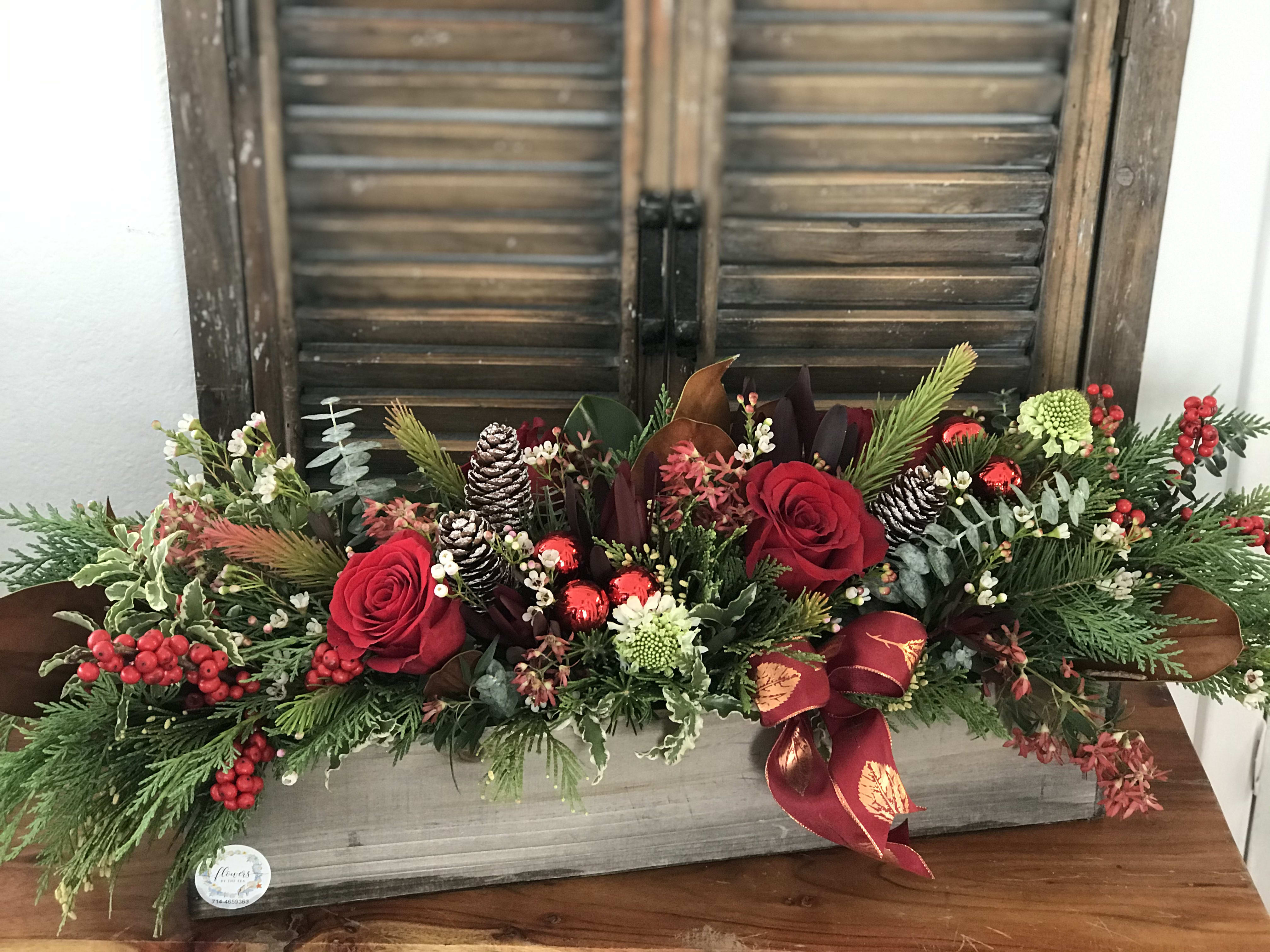 Long holiday centerpiece with red roses, pinecones, and a ribbon in a wooden box