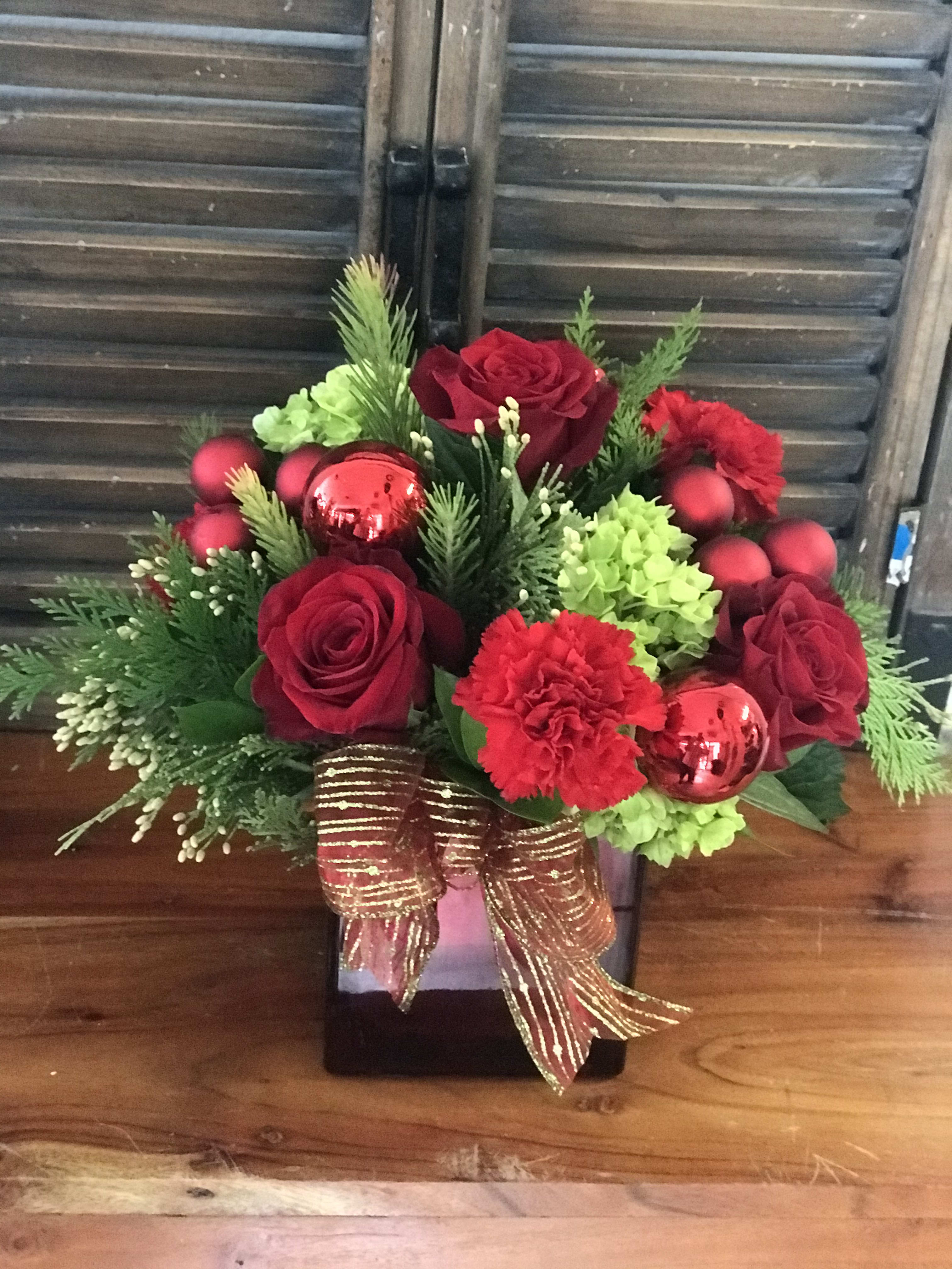 Red roses and carnations in a black vase with green accents and a gold ribbon