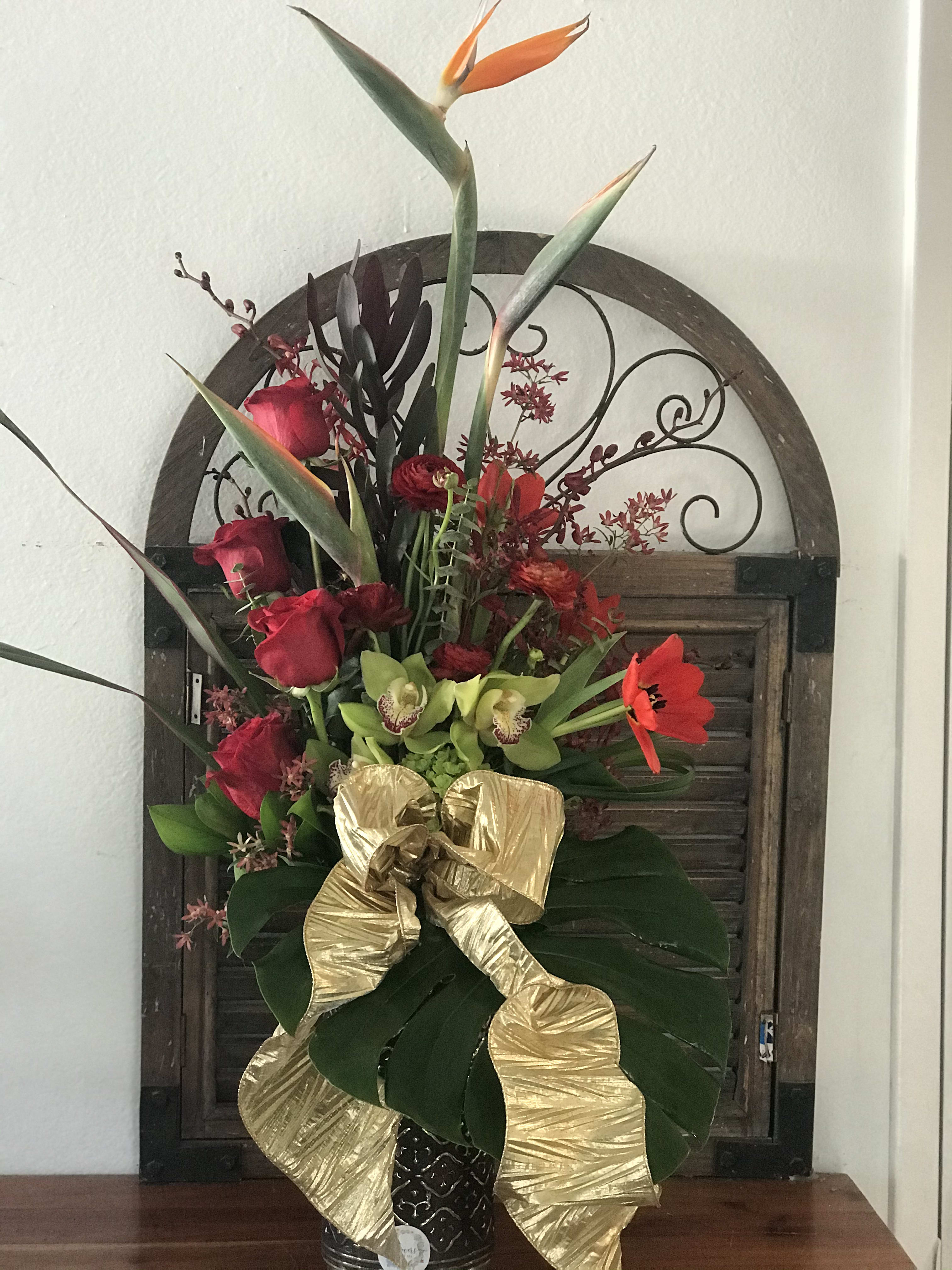 Tall tropical bouquet with red roses, green orchids, and a gold ribbon in a vase