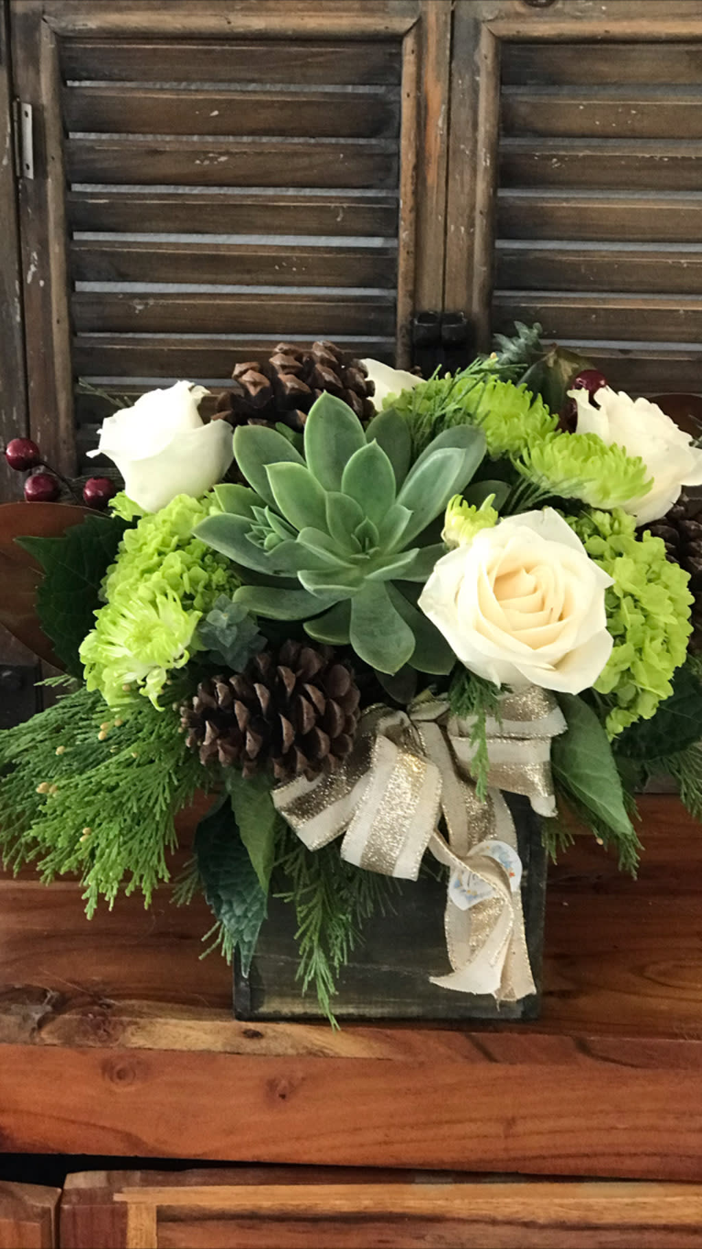 Succulent and white rose arrangement in a dark box with pinecones and ribbon