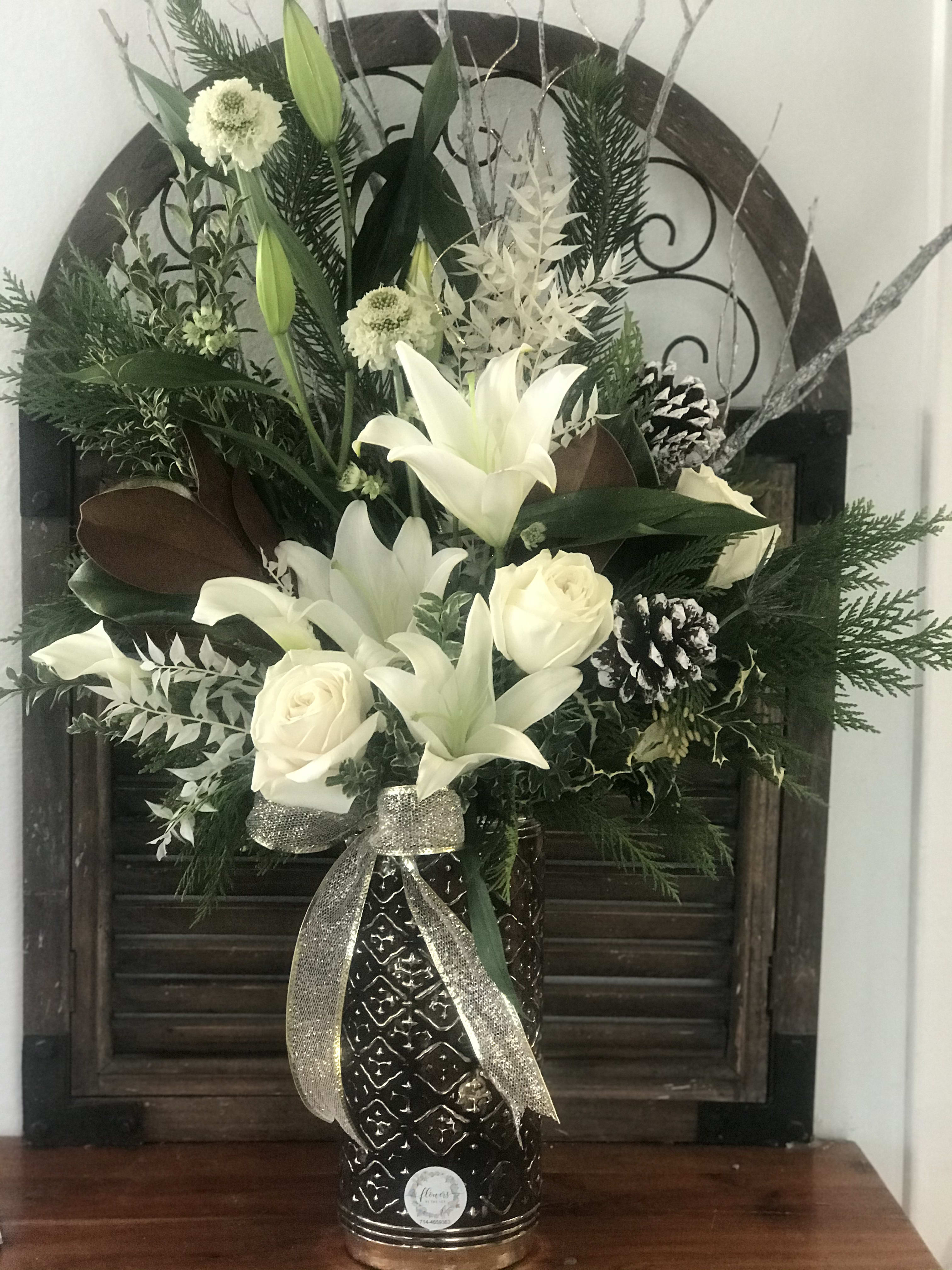 White lilies and roses in a dark vase with a silver ribbon