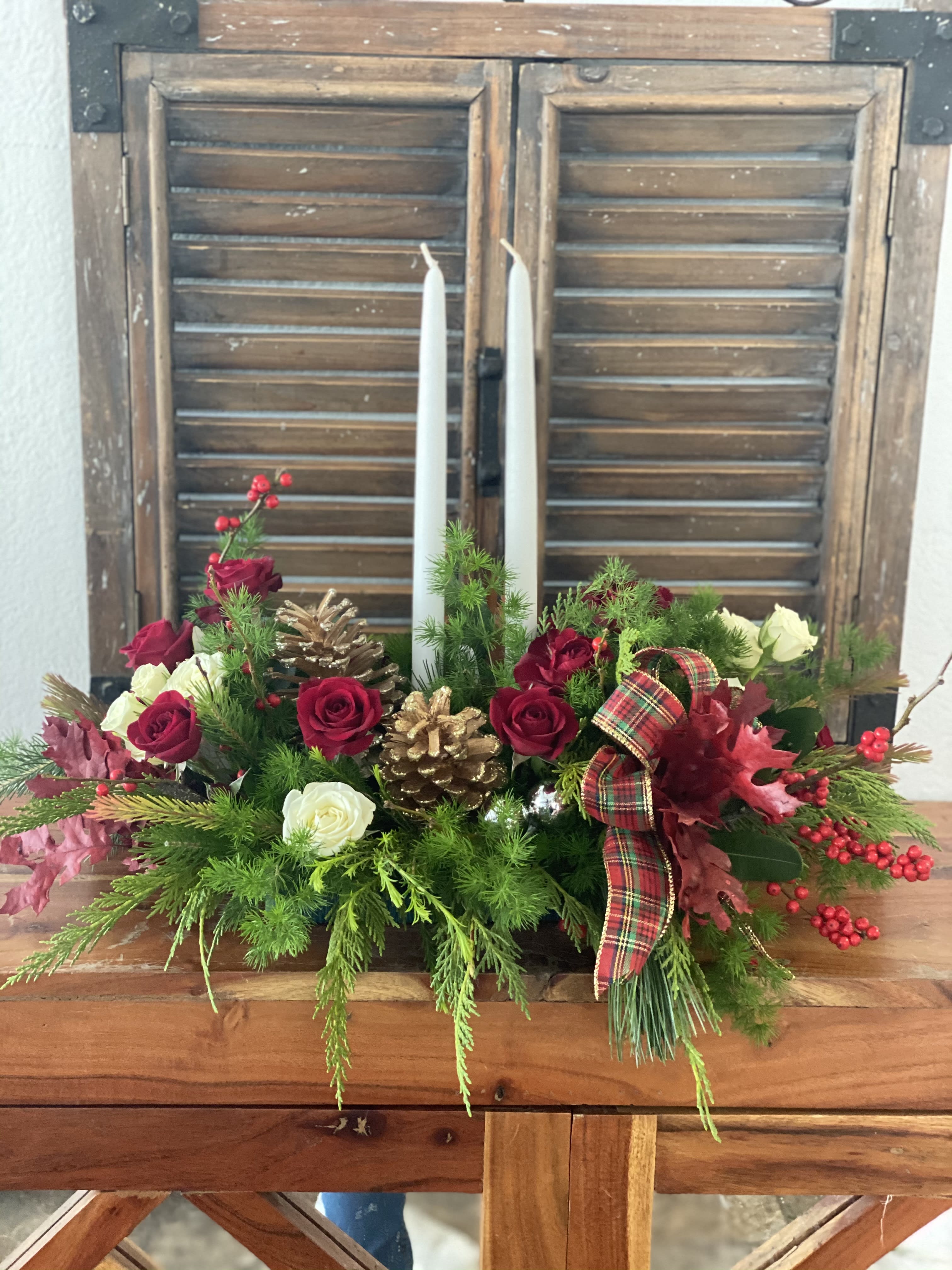 Holiday centerpiece with red and white roses, pinecones, and two white taper candles