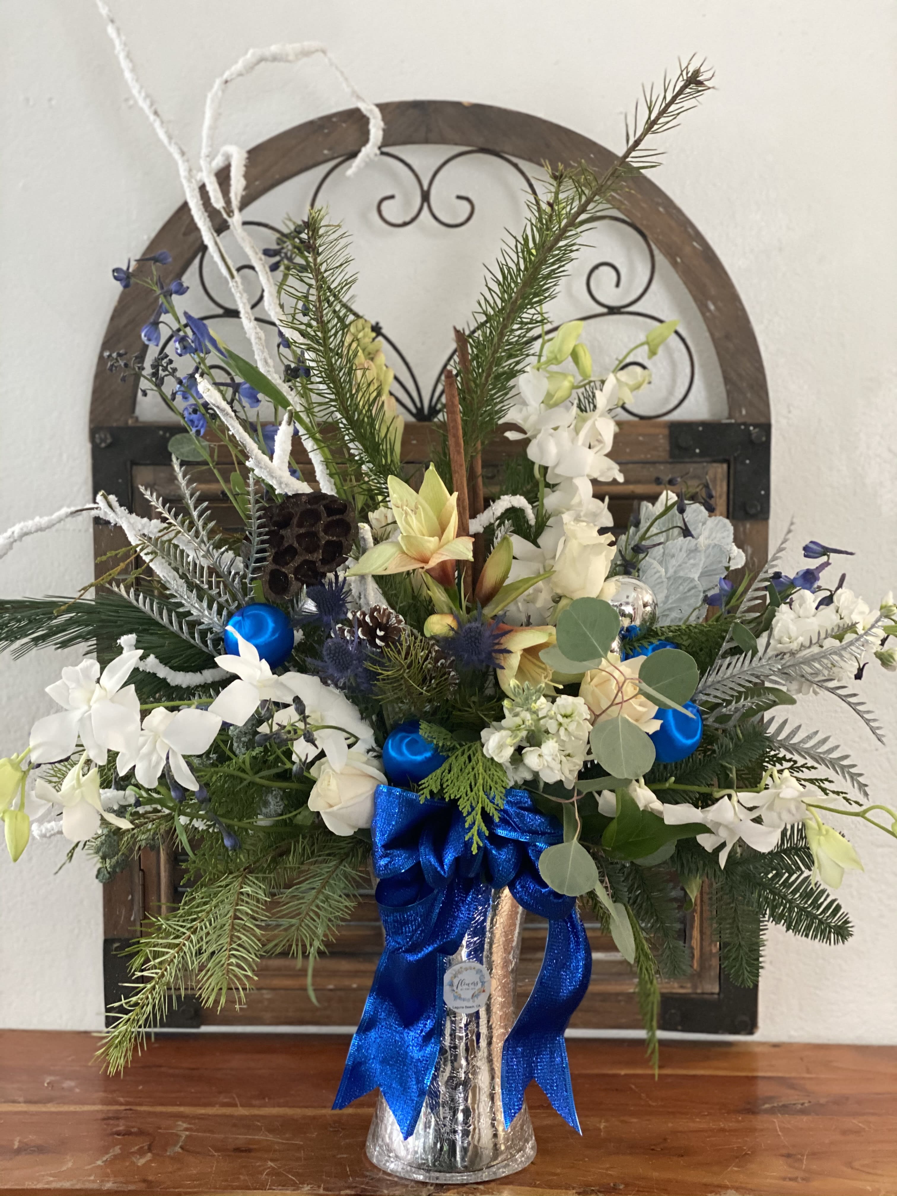 Holiday floral arrangement in a silver vase with blue ribbon and white blooms