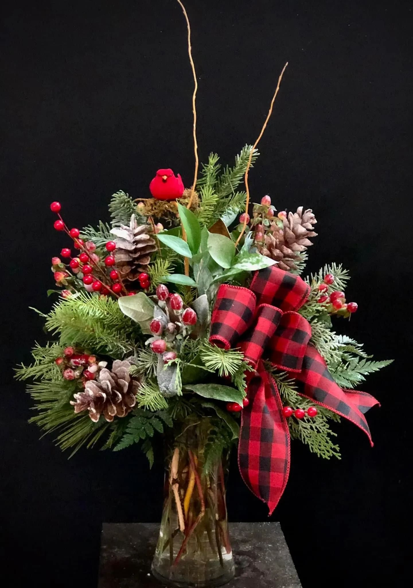Holiday arrangement with pinecones, berries, and a red plaid ribbon in a glass vase
