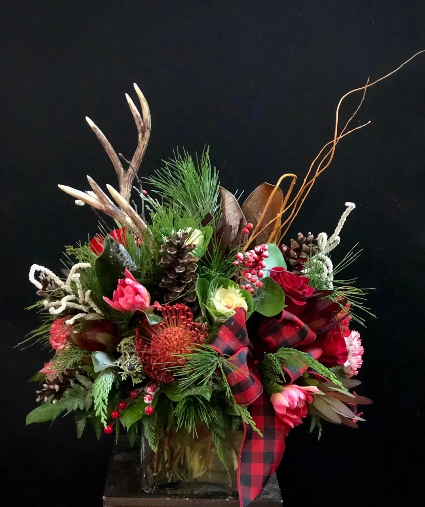Holiday floral arrangement in a glass vase with pinecones, berries, and plaid ribbon