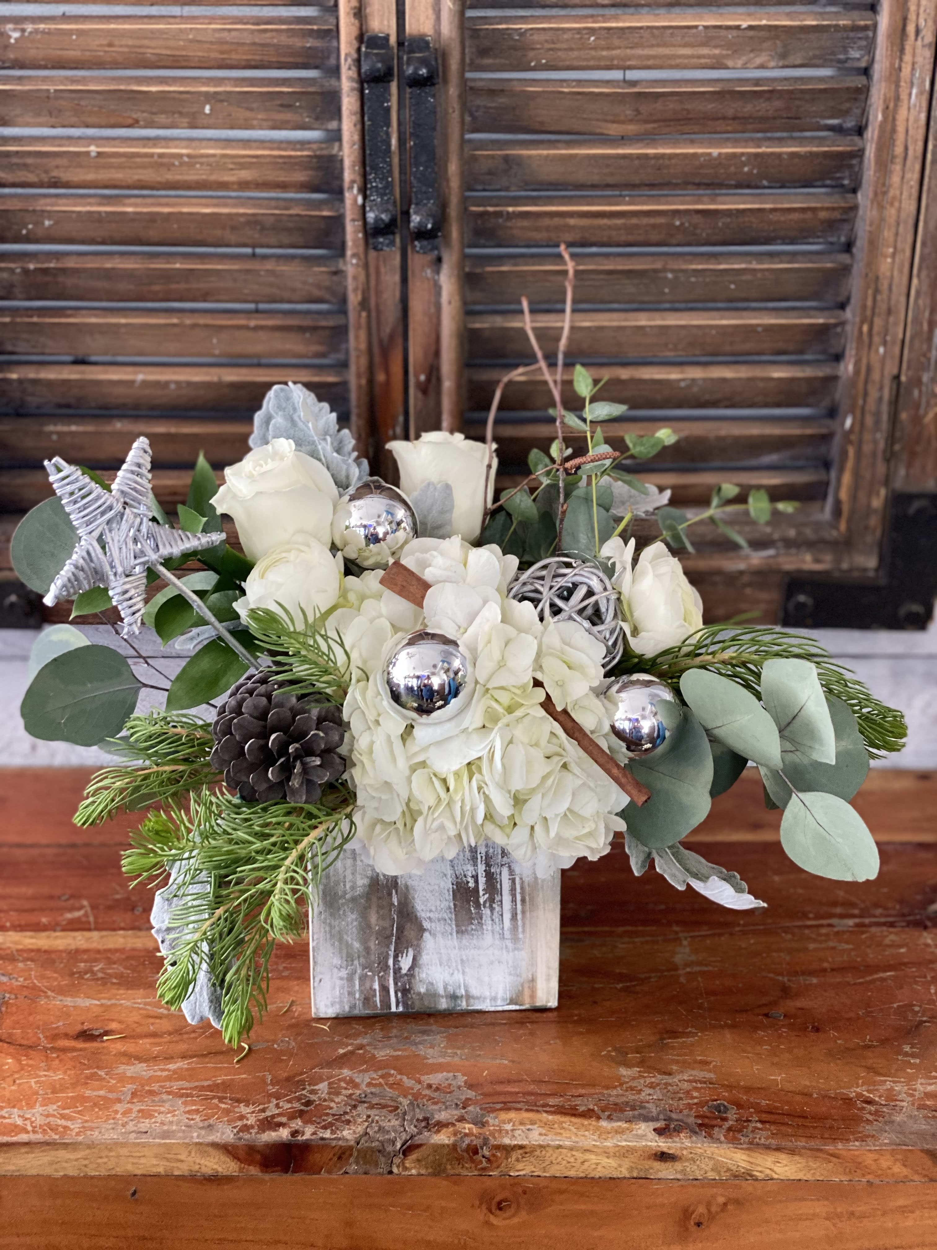 White floral arrangement in a rustic wooden box with pinecones and silver ornaments