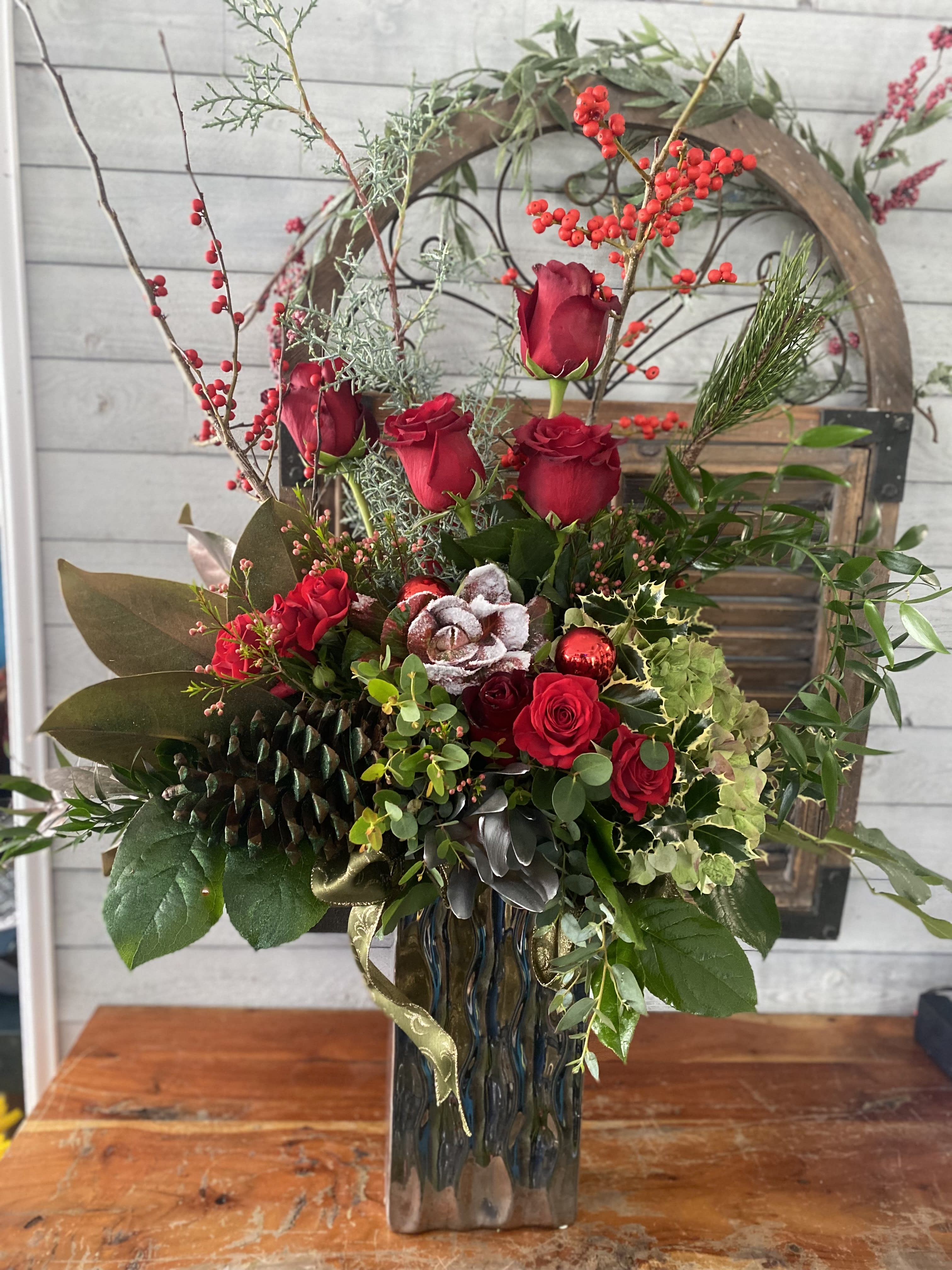 Red roses and berries arranged in a tall glass vase with holiday greenery