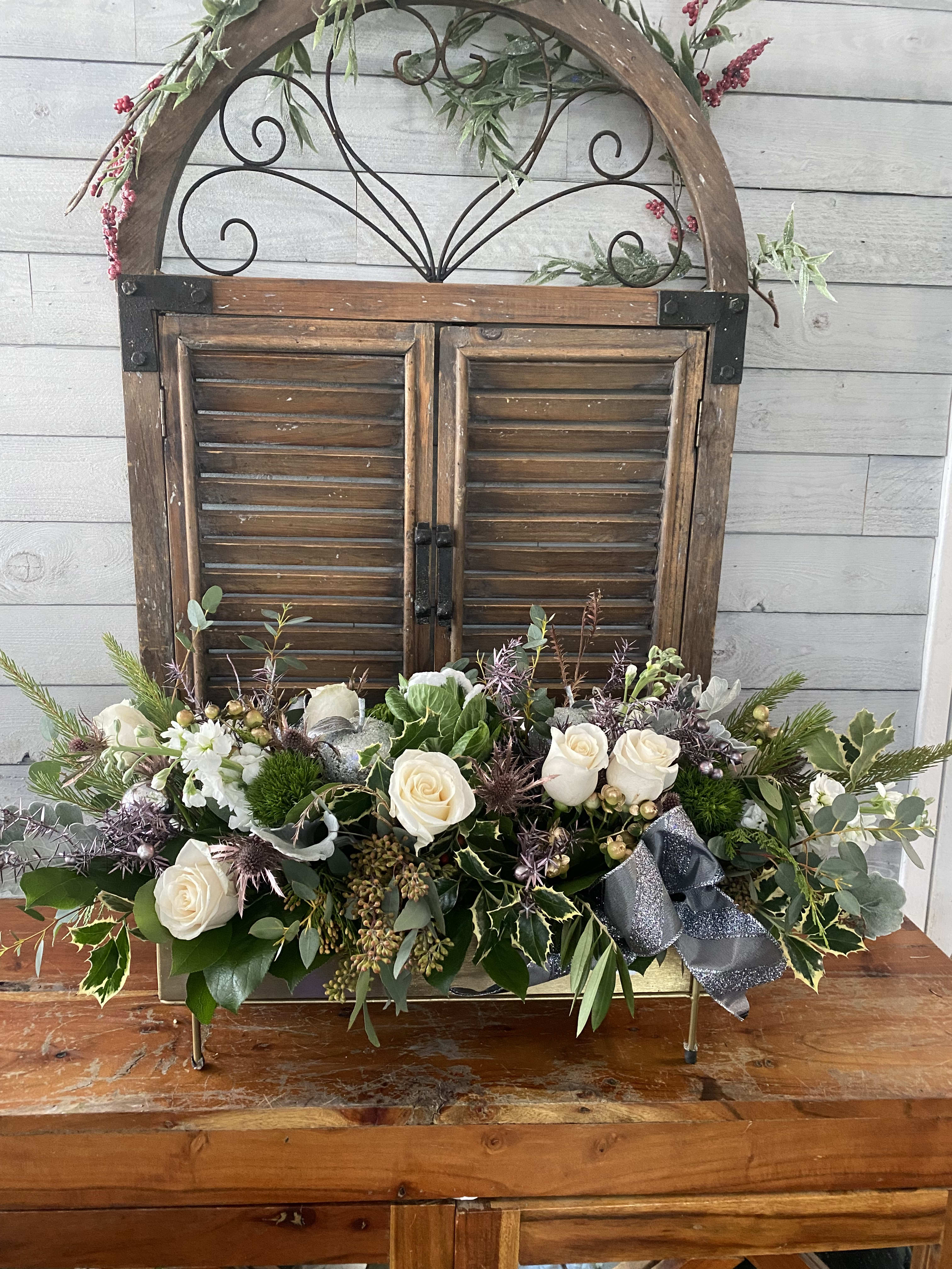 White roses in a low floral arrangement with greenery and a silver ribbon