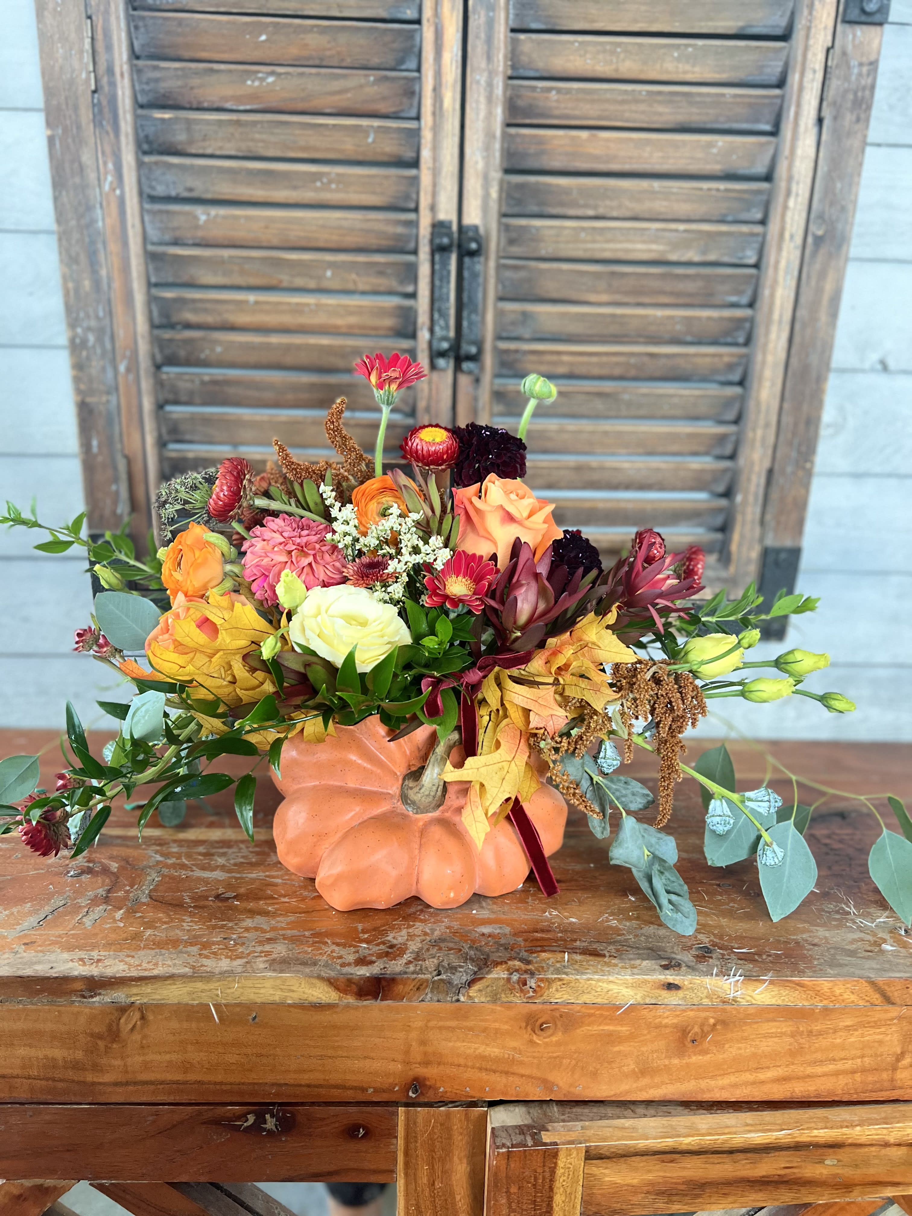 Autumn floral arrangement in a pumpkin-shaped container with orange, pink, and burgundy blooms