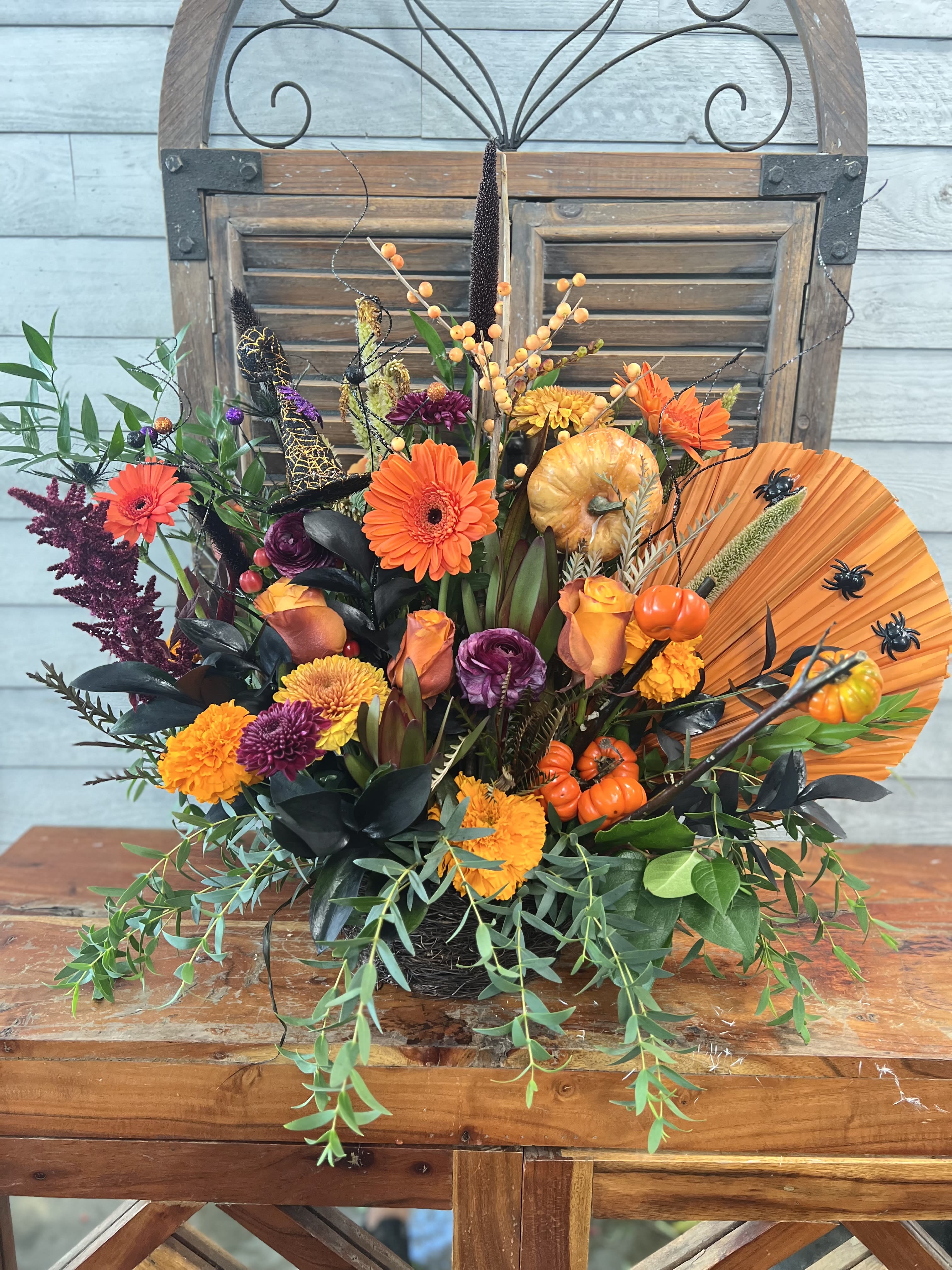 Autumn floral arrangement with orange and purple blooms, pumpkins, and a fan accent