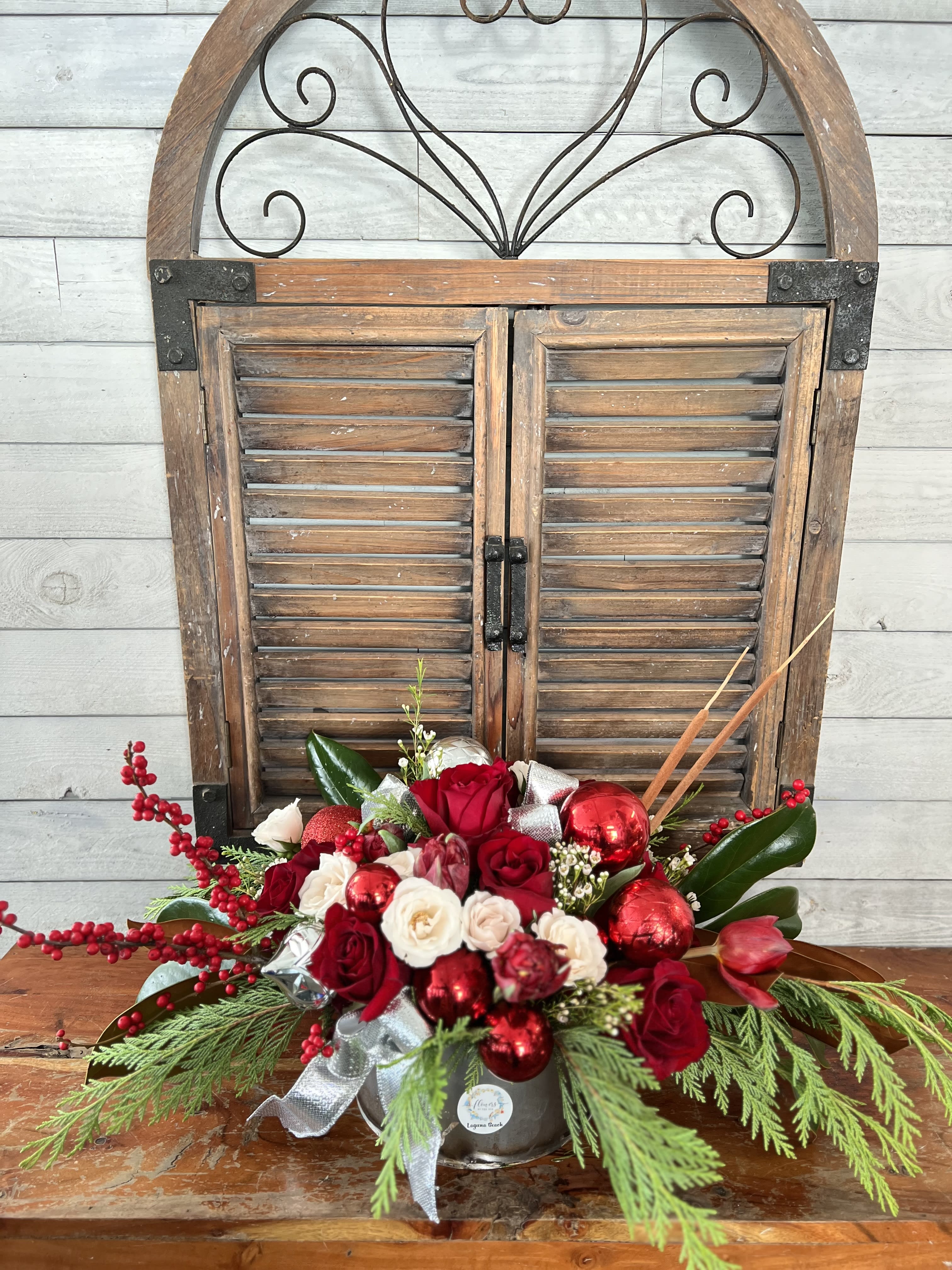 Red and white rose arrangement with holiday ornaments in a silver container