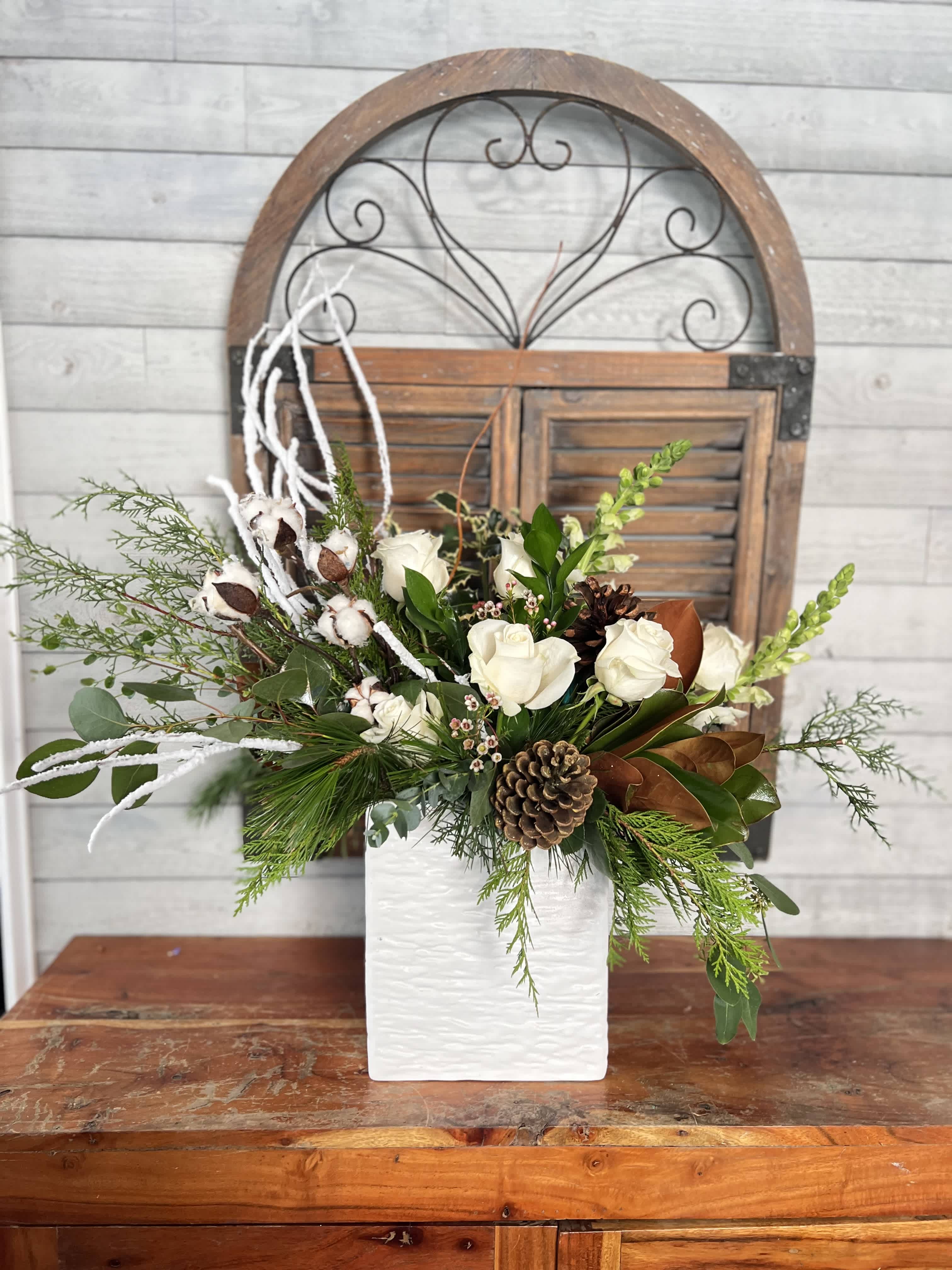 White roses in a white vase with pinecones and greenery