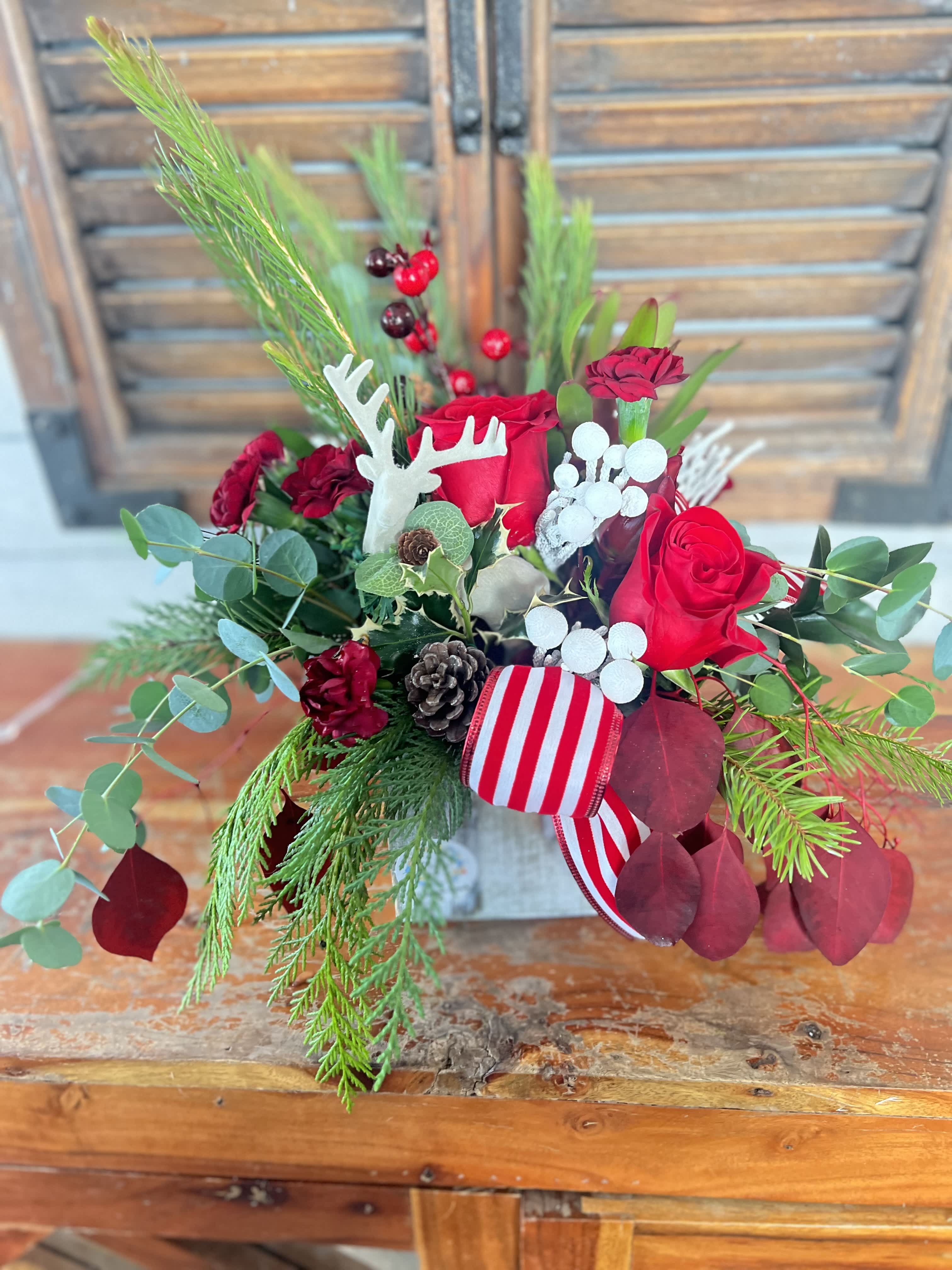 Red rose arrangement with pine, berries, and a striped ribbon in a rustic container