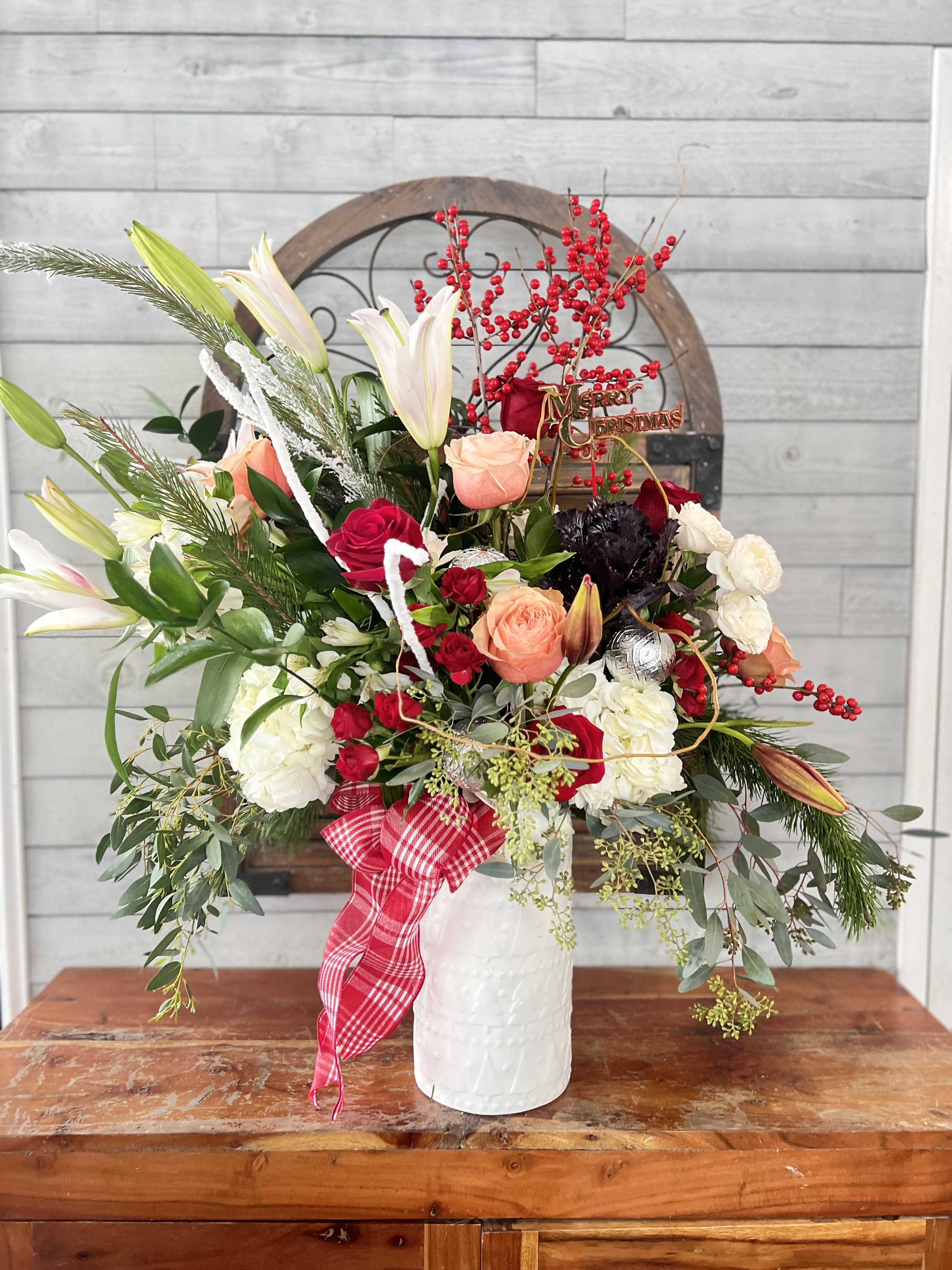 Christmas floral arrangement in a white vase with lilies, roses, and red berries