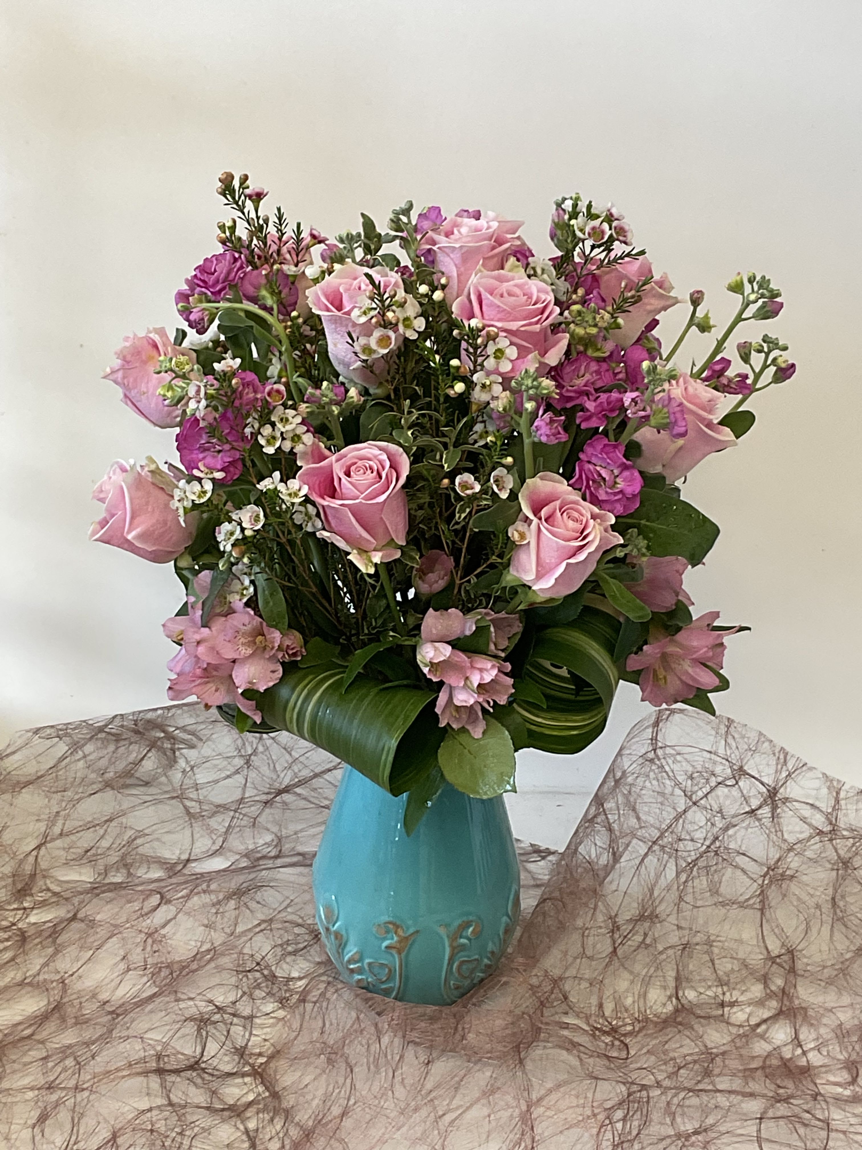 Pink roses and small purple flowers arranged in a turquoise vase