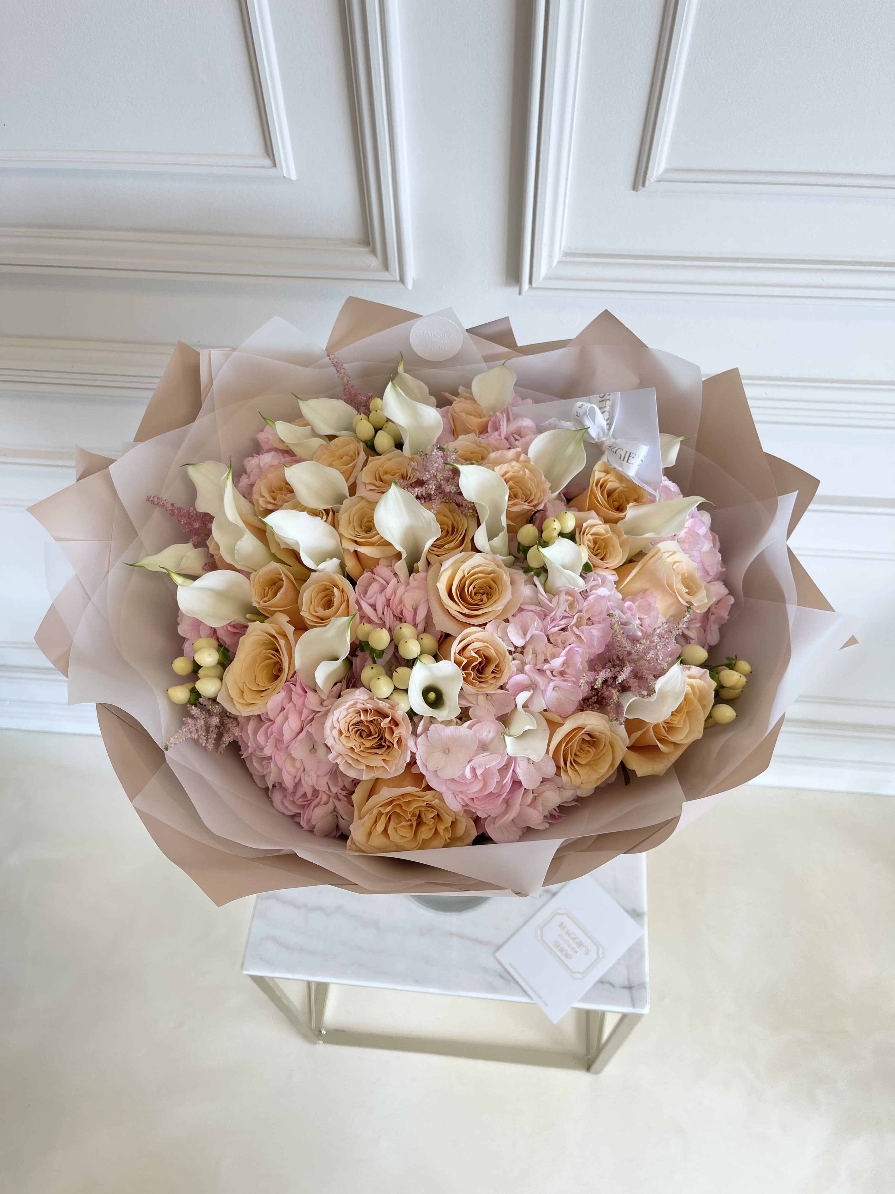Bouquet of peach roses, pink hydrangeas, and white calla lilies wrapped in blush paper
