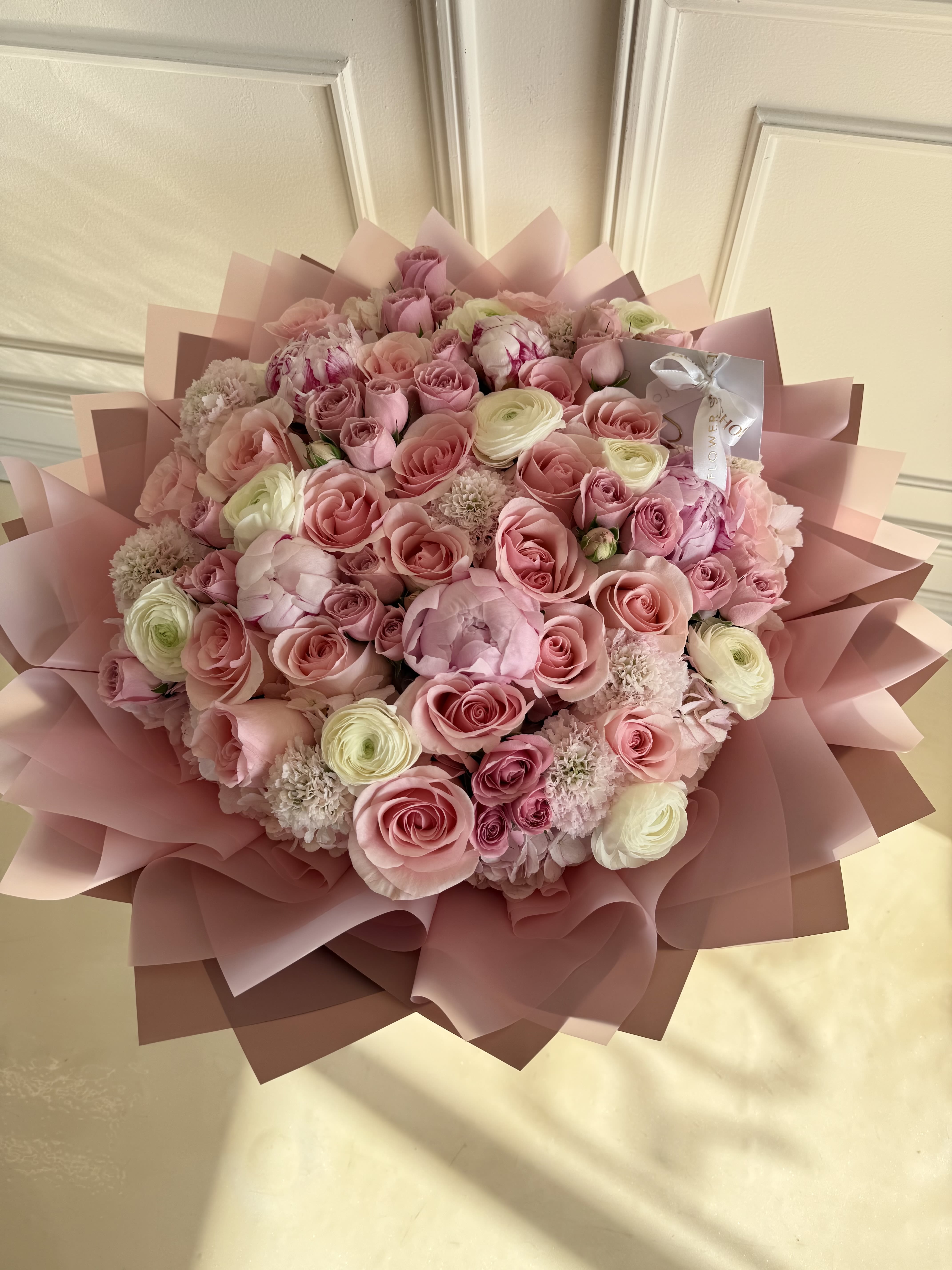 Large pink bouquet of roses and ranunculus wrapped in pink paper