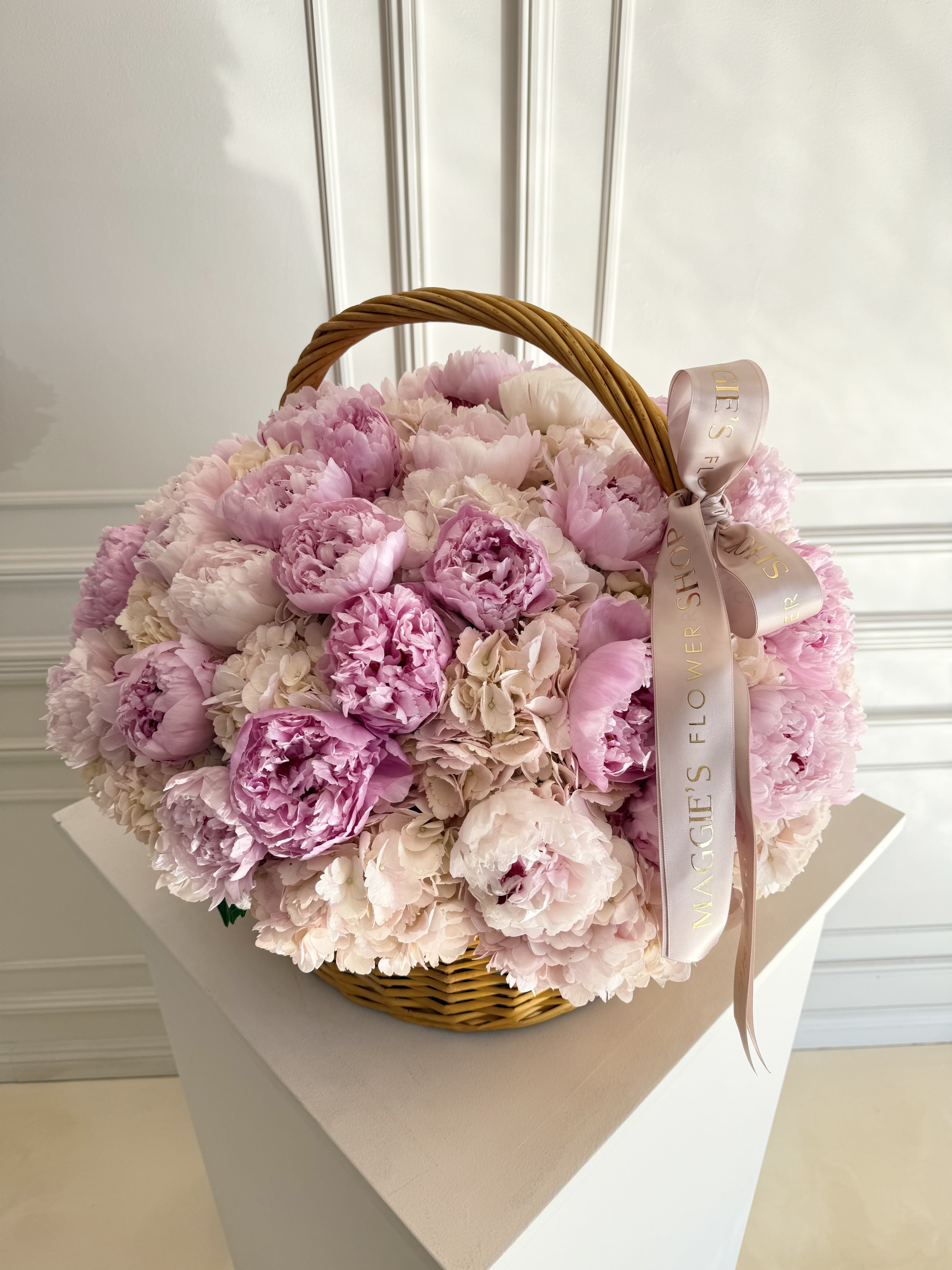 Pink peonies in a wicker basket with a ribbon bow