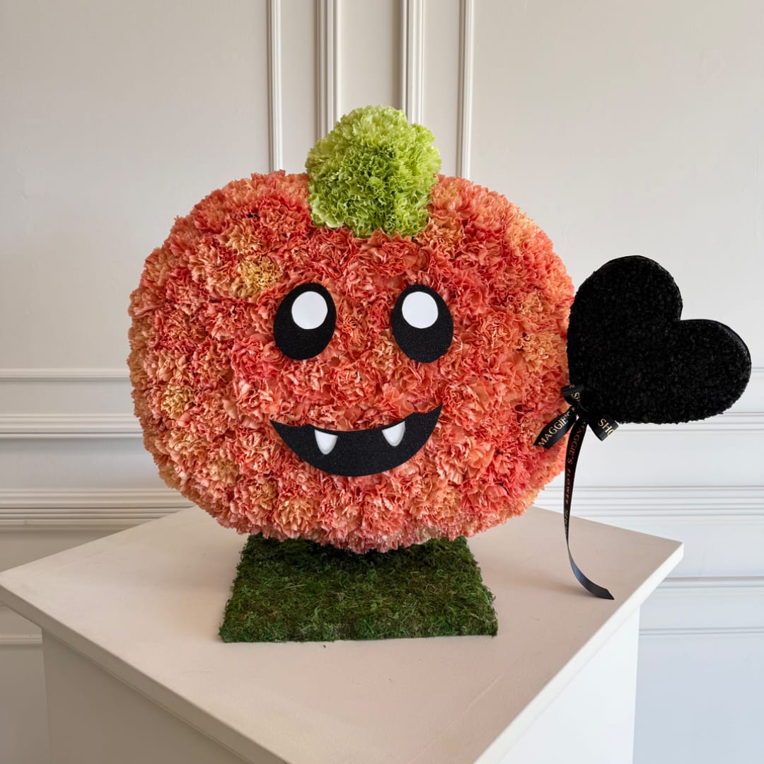 Pumpkin-shaped floral arrangement with a black heart accent on a moss base