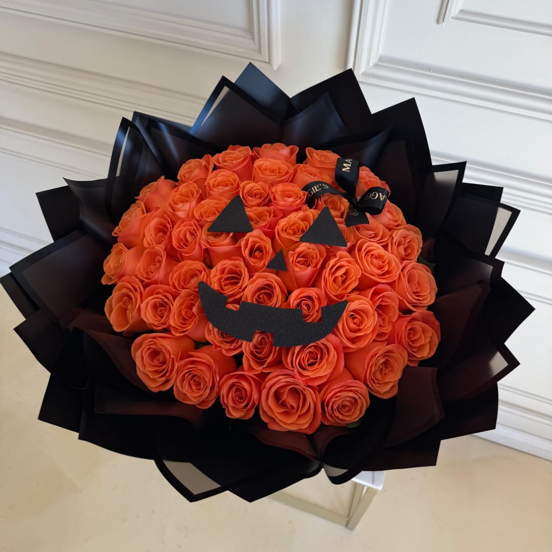 Orange rose bouquet wrapped in black paper with a jack-o'-lantern face