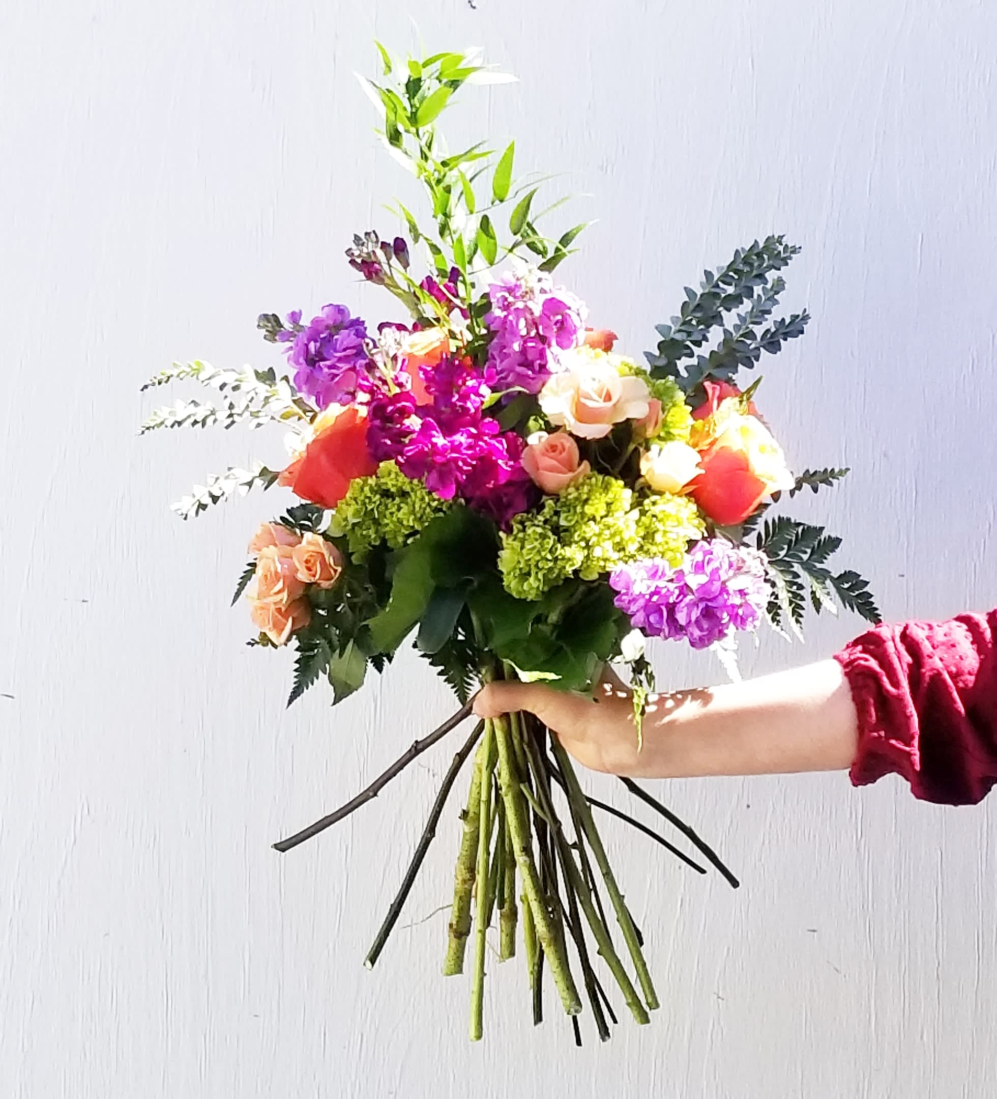 Handheld bouquet of mixed pink, purple, and peach flowers