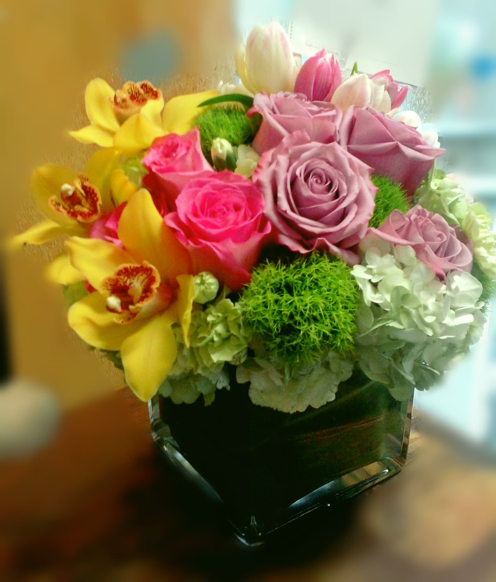 Bouquet of pink roses and yellow orchids in a square glass vase