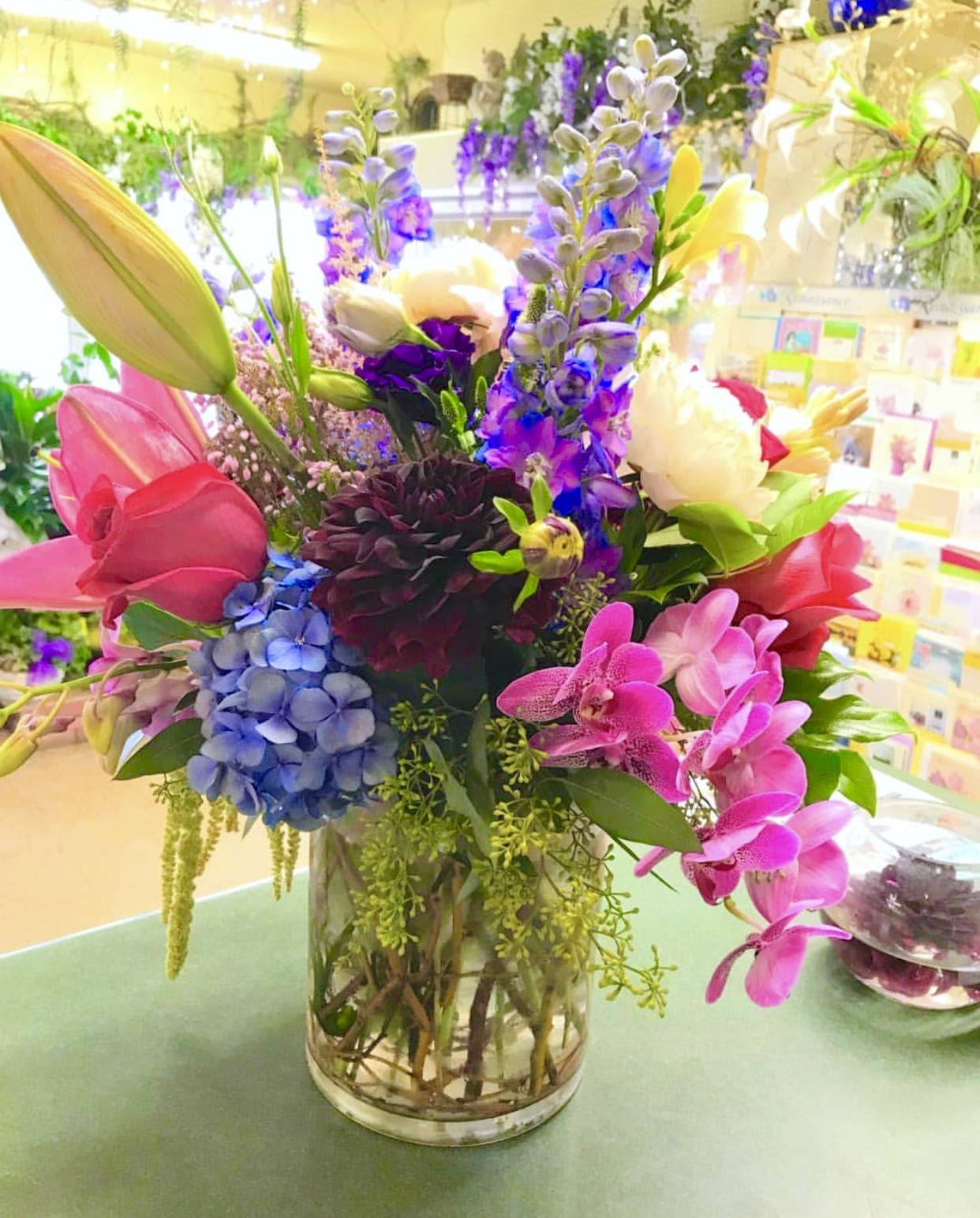 Colorful mixed bouquet in a clear glass vase with lilies, orchids, and hydrangeas