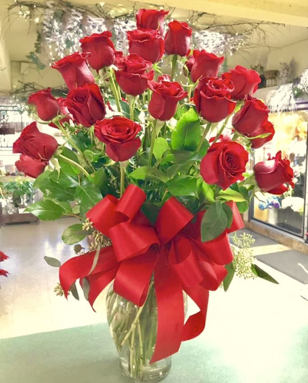 Tall bouquet of red roses in a glass vase with a large red ribbon