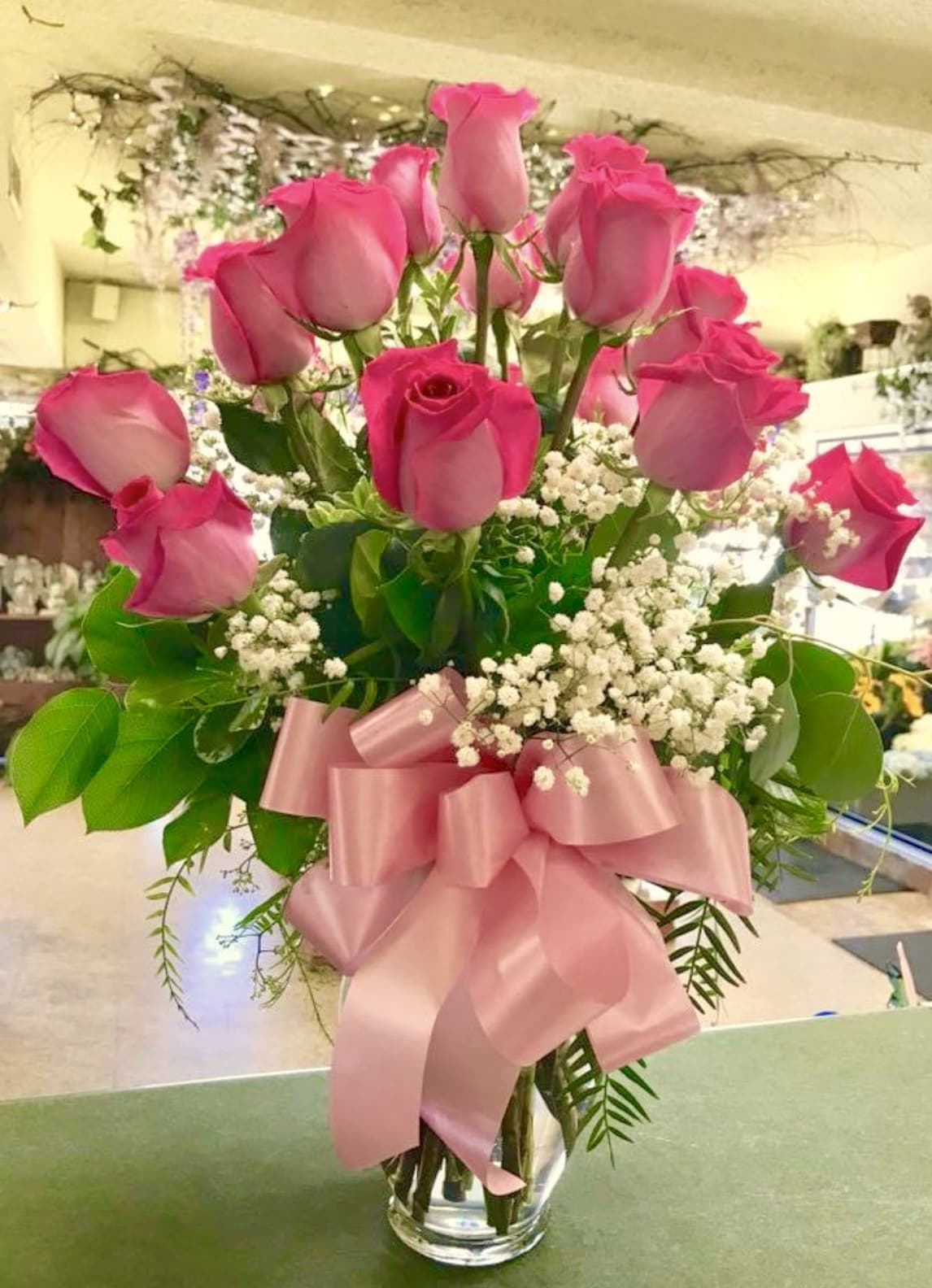 Pink roses arranged in a clear glass vase with a pink ribbon bow