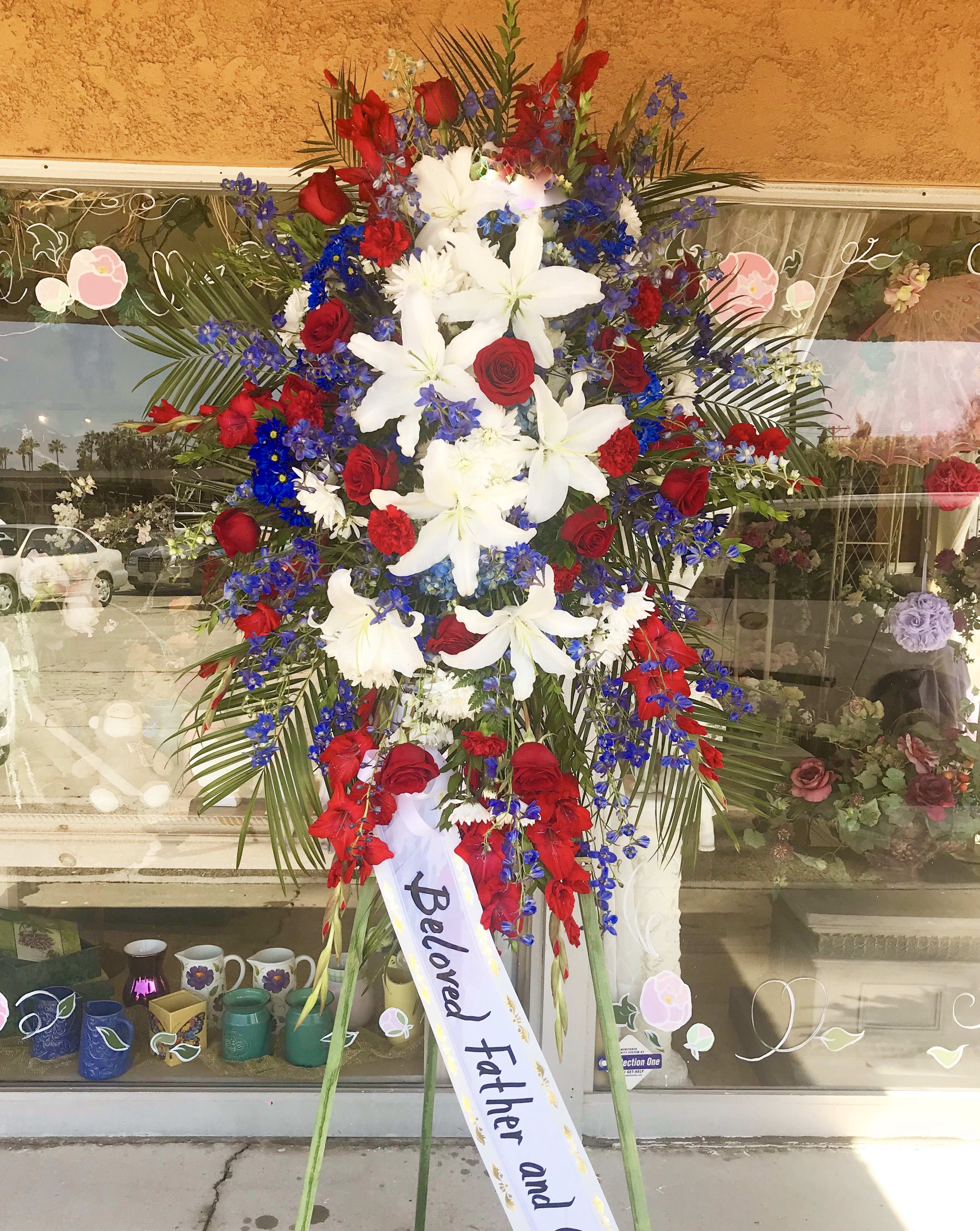Standing funeral spray with red roses, white lilies, and blue flowers