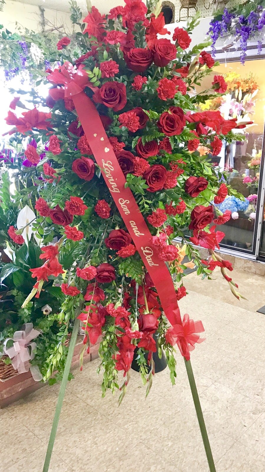 Large standing floral spray of red roses and carnations with a red ribbon