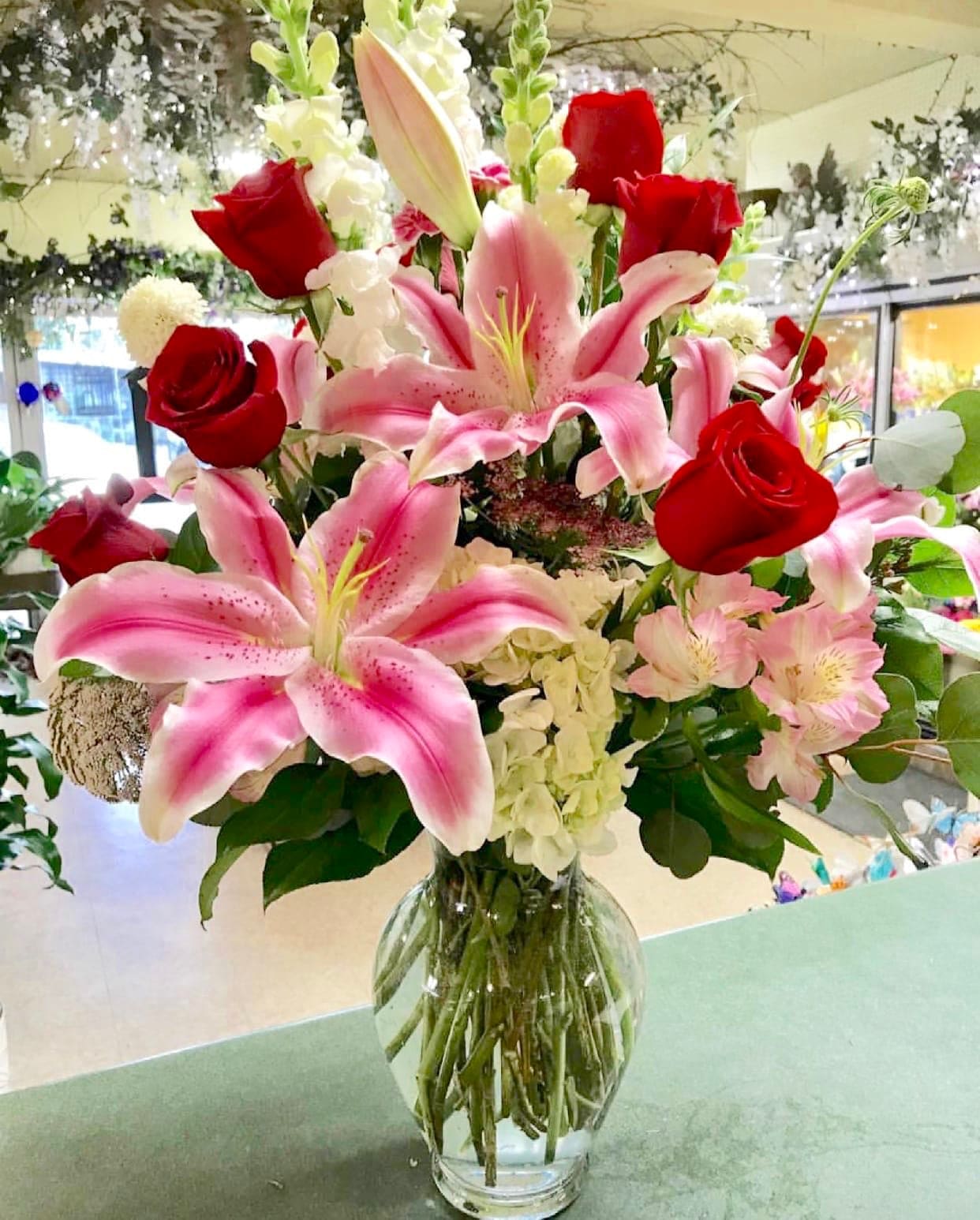 Blow Me Away - A stunning arrangement of premium red roses and blooming and vibrant lilies complemented by accenting snapdragons, hydrangea and alstroemerias in a 11” clear glass vase