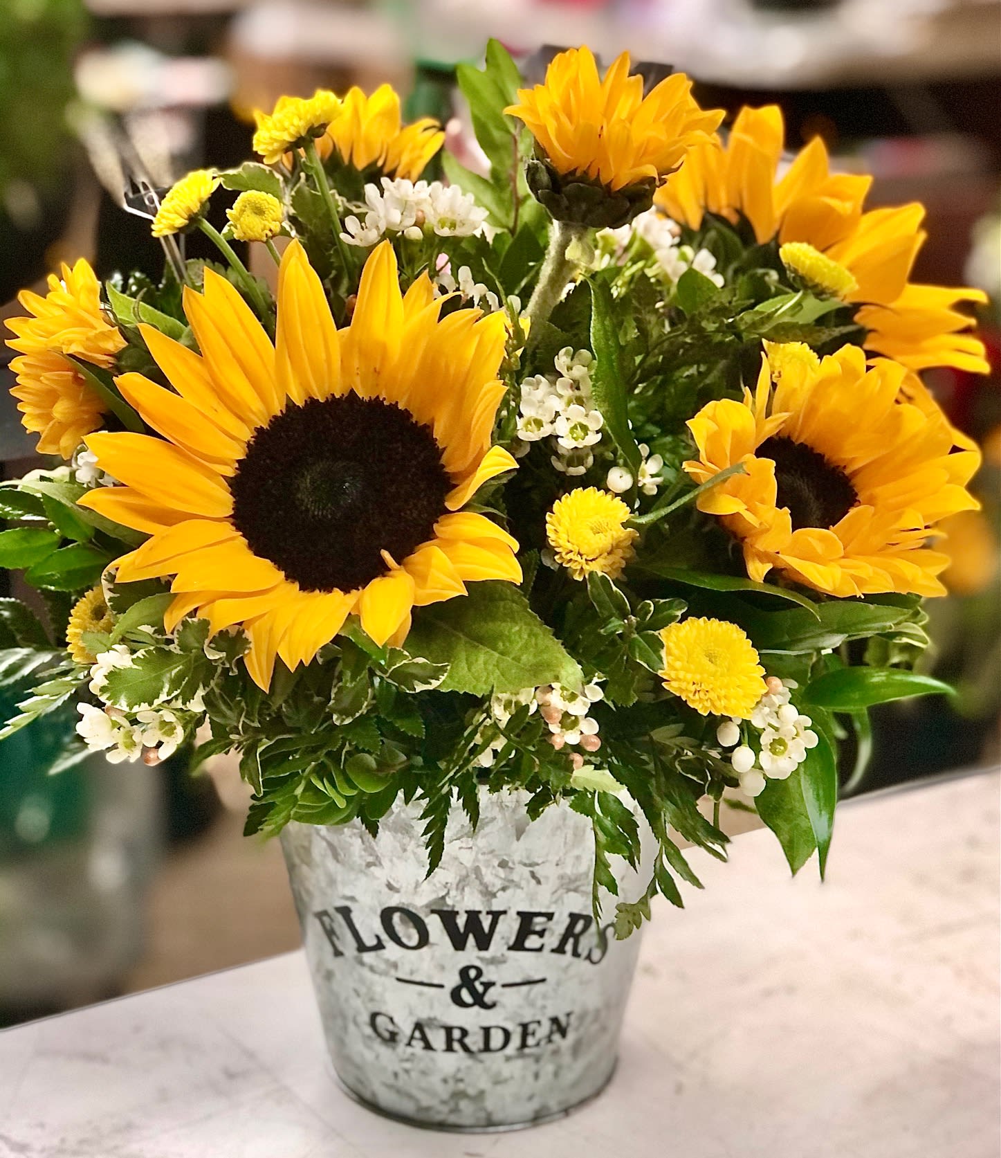 Bouquet of yellow sunflowers and small white flowers in a metal container