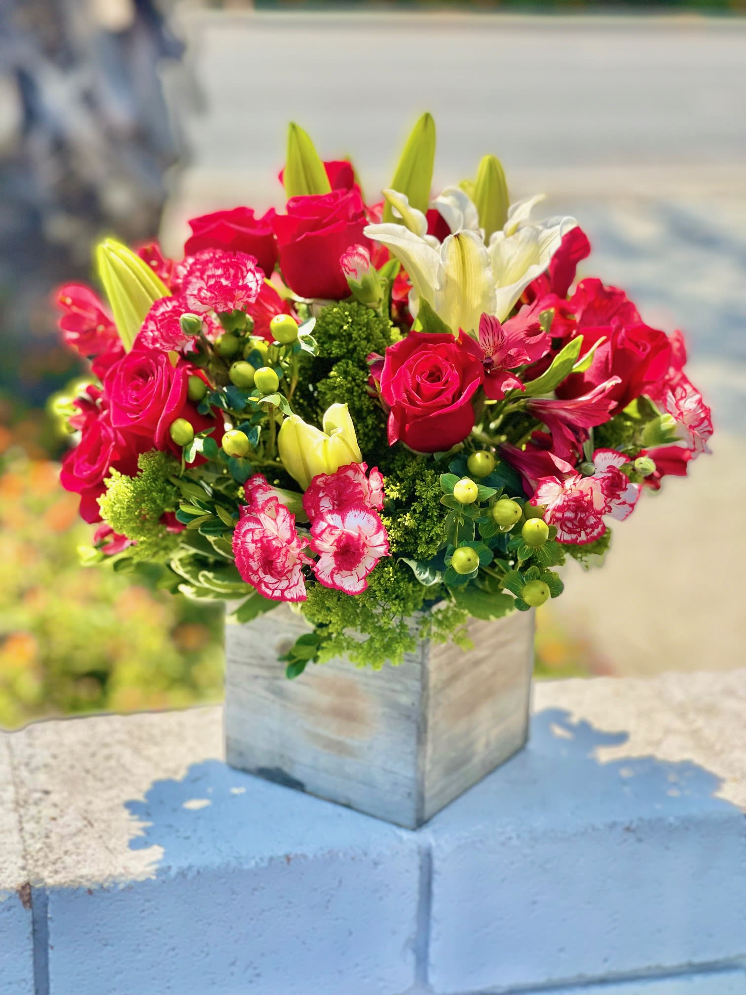Bouquet of red roses, white lilies, and pink carnations in a square vase